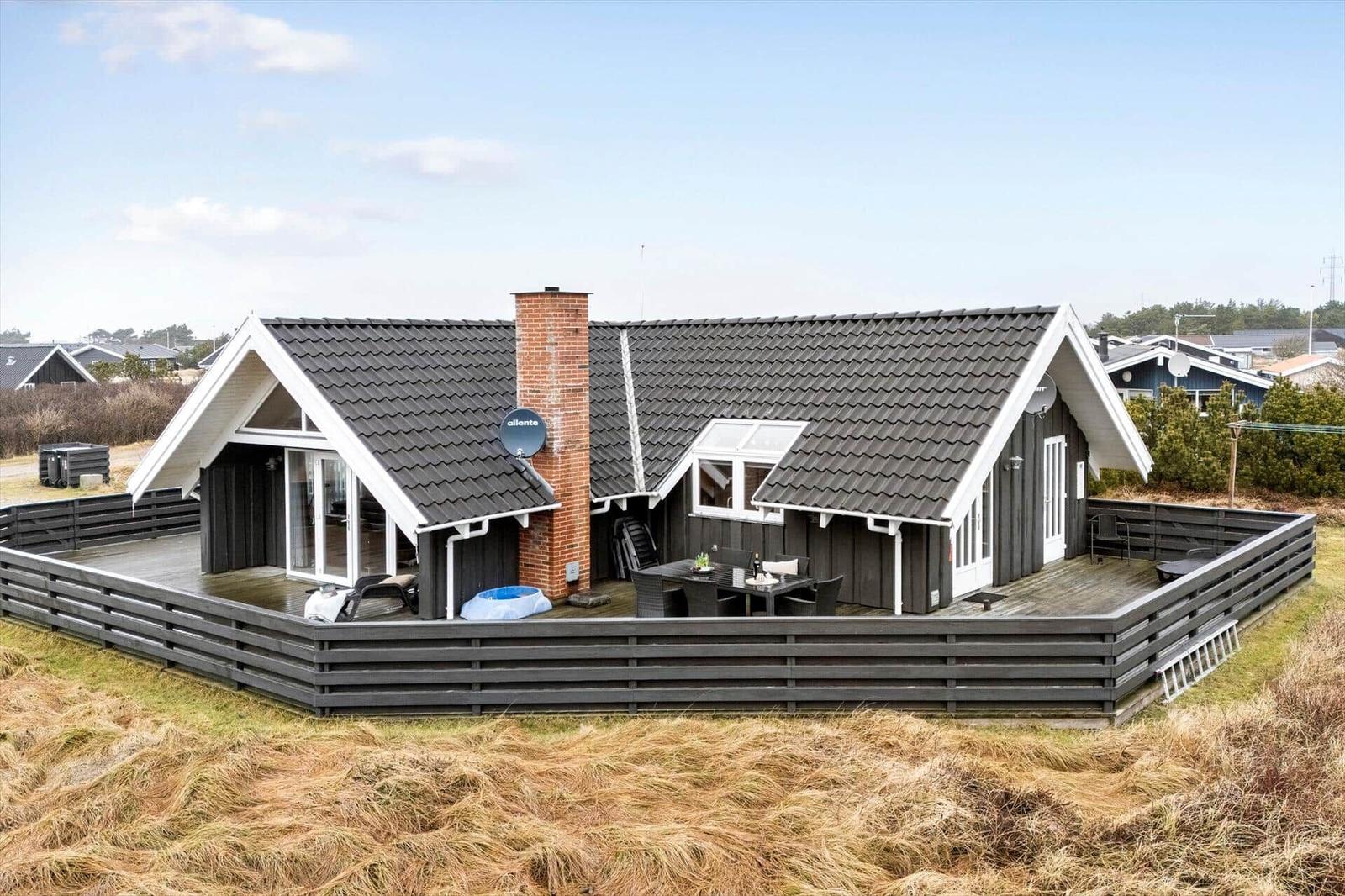 Moderne Ferienhaus mit großem Holzterrasse und Grillplatz im Freien.