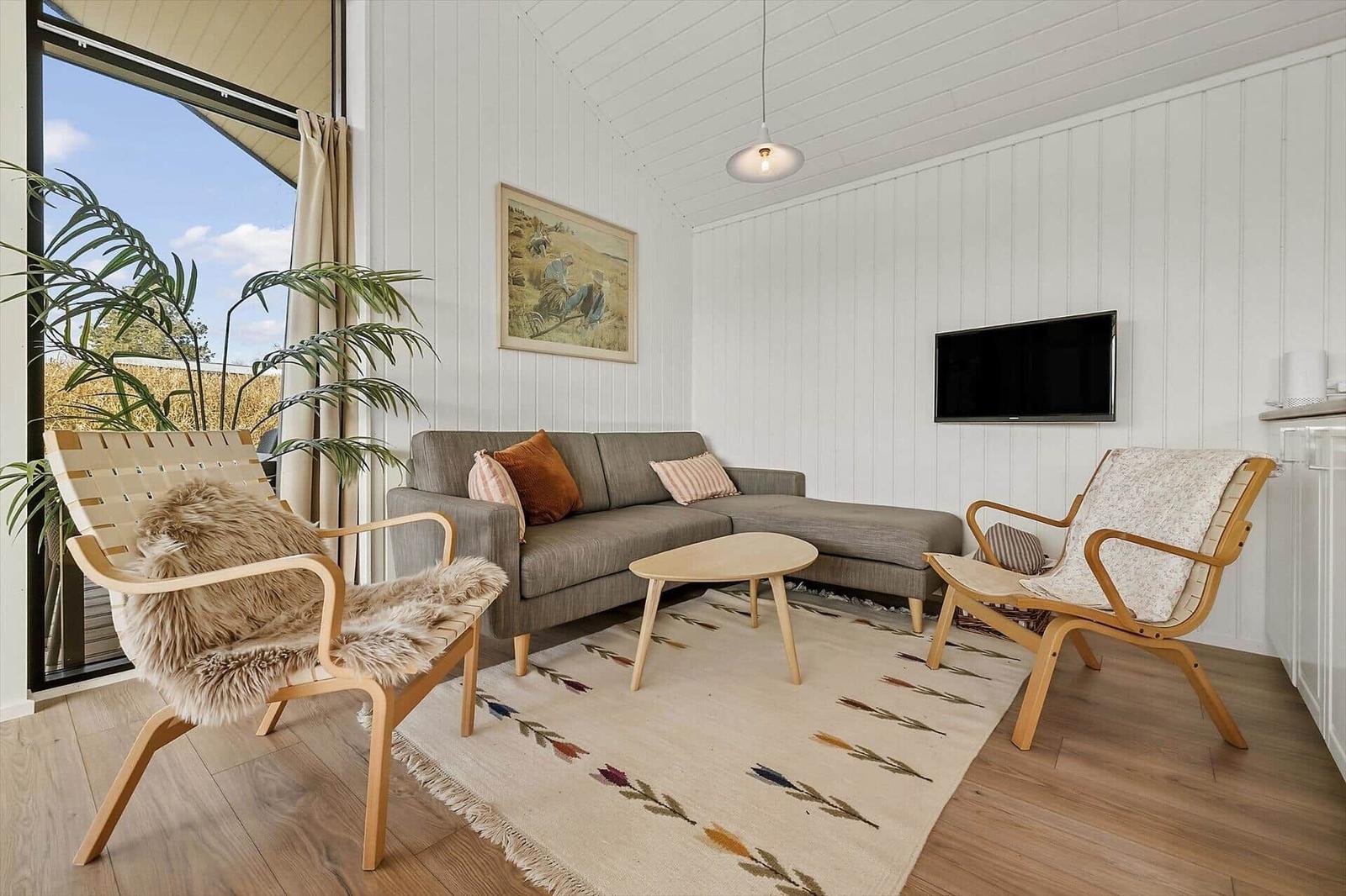 Wohnzimmer mit Sofa, zwei Stühlen, Teppich und Fernseher an der Wand.
