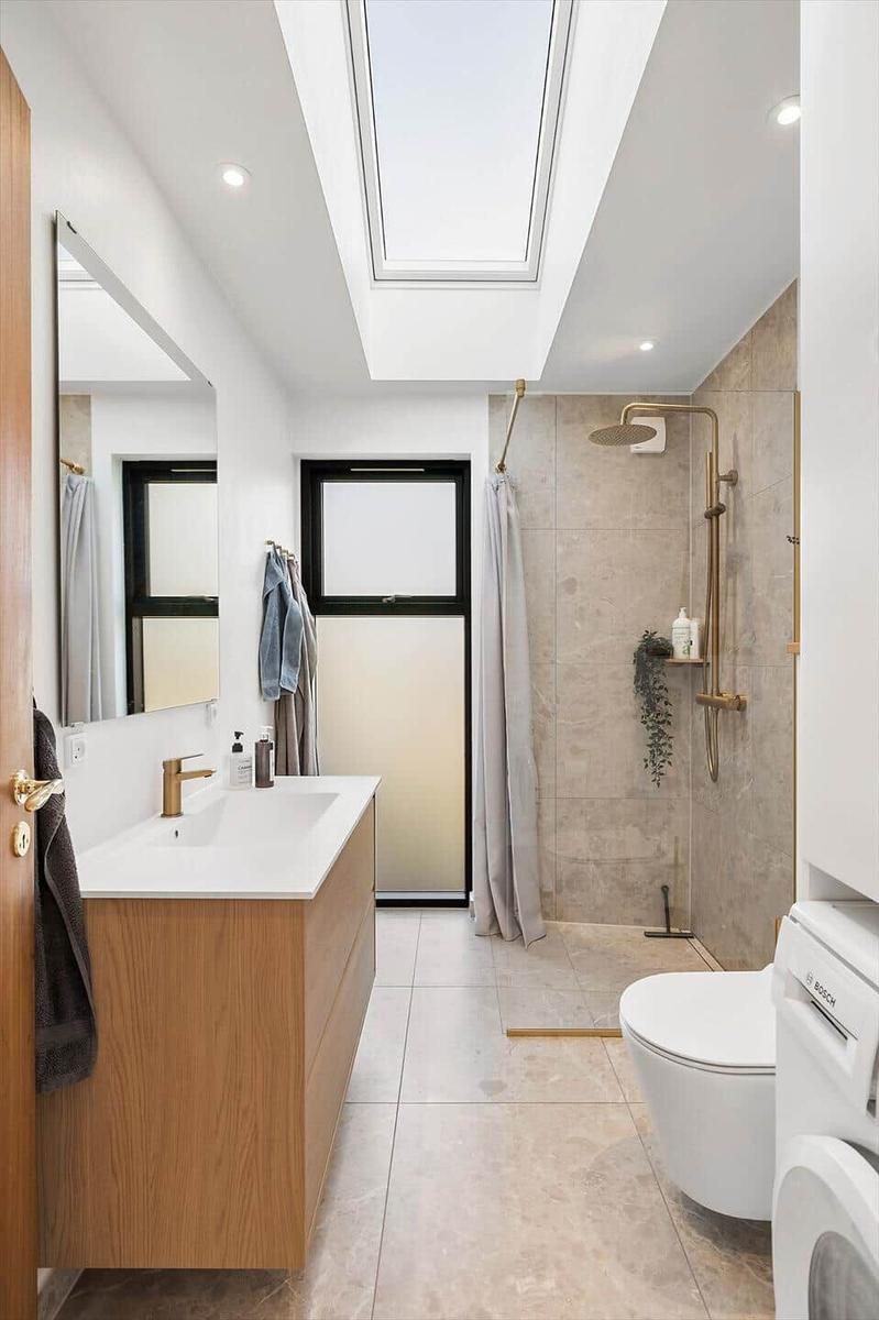 Badezimmer mit Dusche, Waschbecken und Toilette unter Dachfenster.