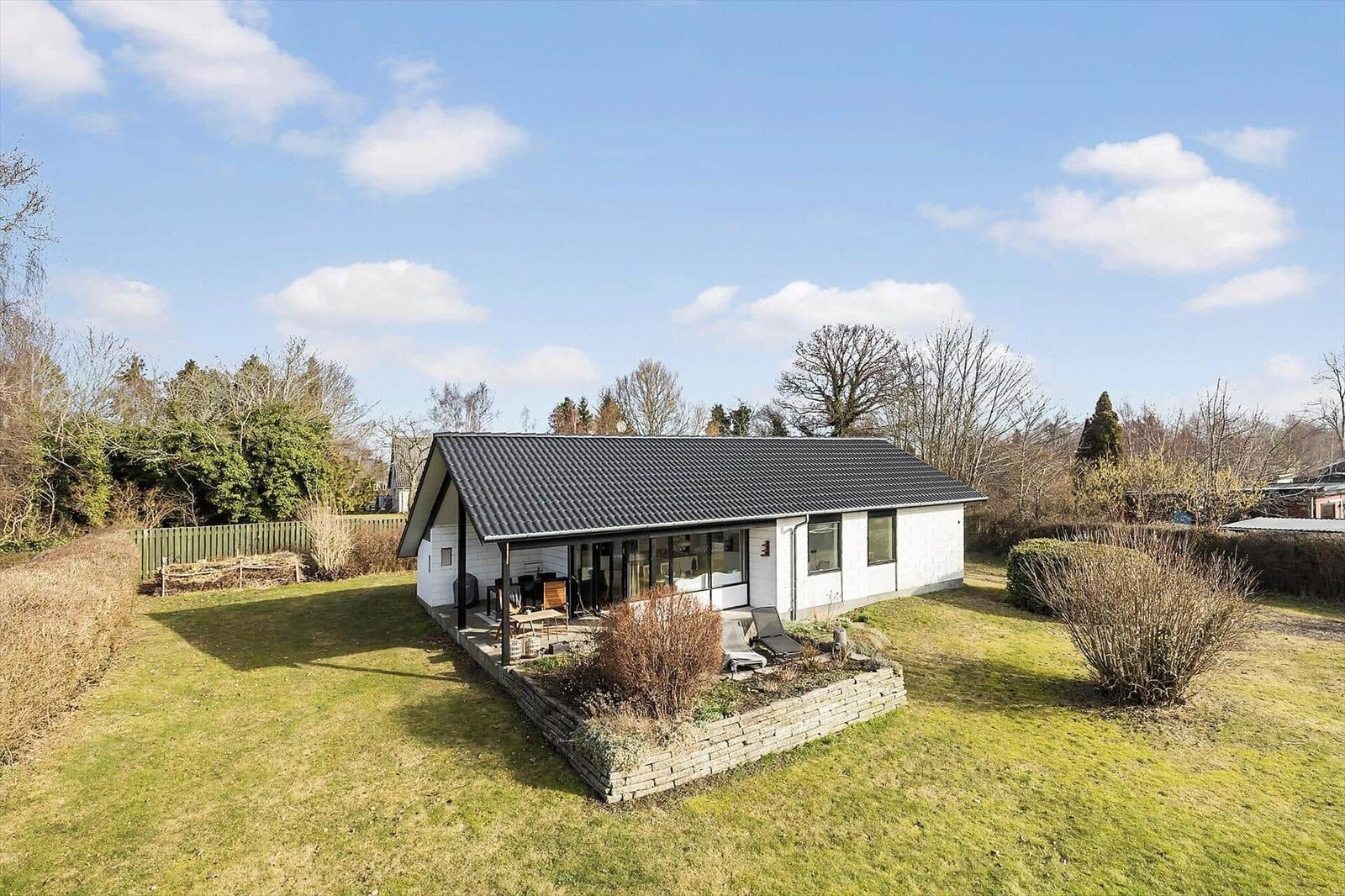 Moderne Villa mit großem Garten und Terrasse unter blauem Himmel.
