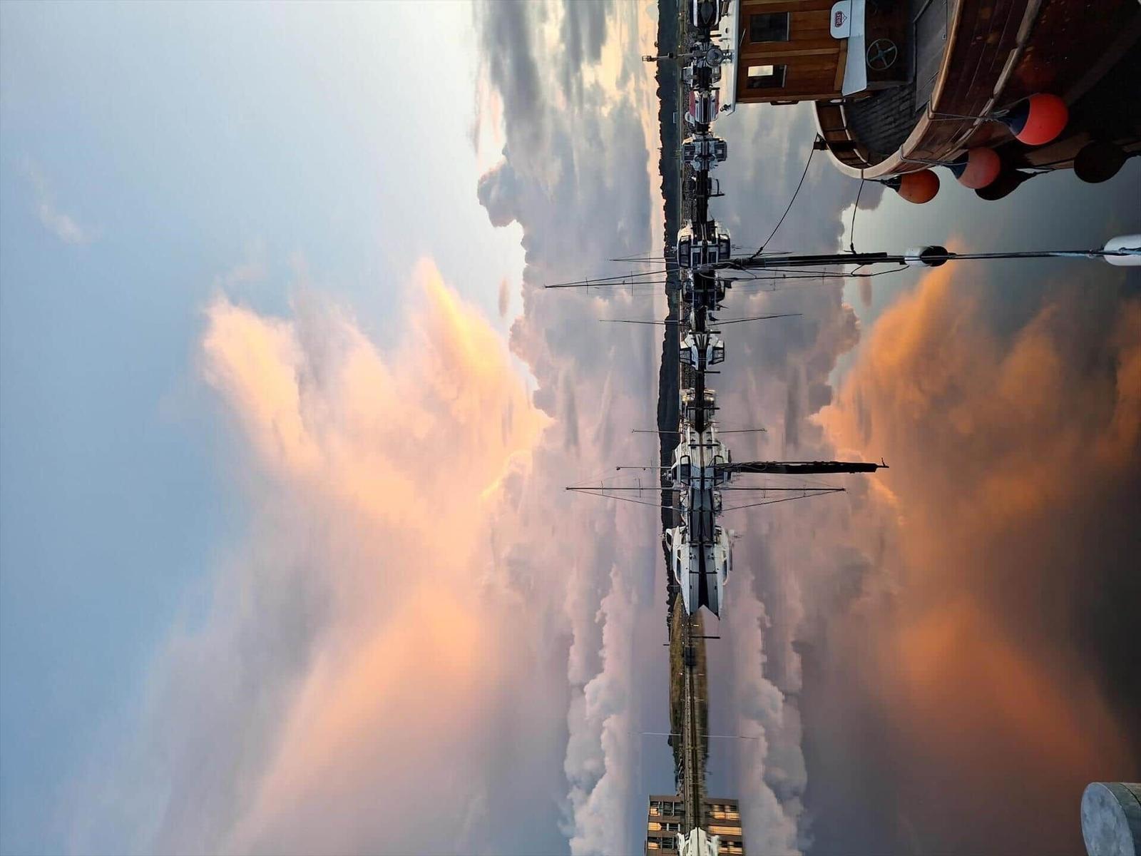 Bootshäuser und Segelboote am Hafen bei Sonnenuntergang.