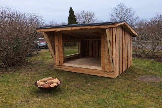 Holzkonstruktion mit Sitzbank und Kaminbereich im Freien.