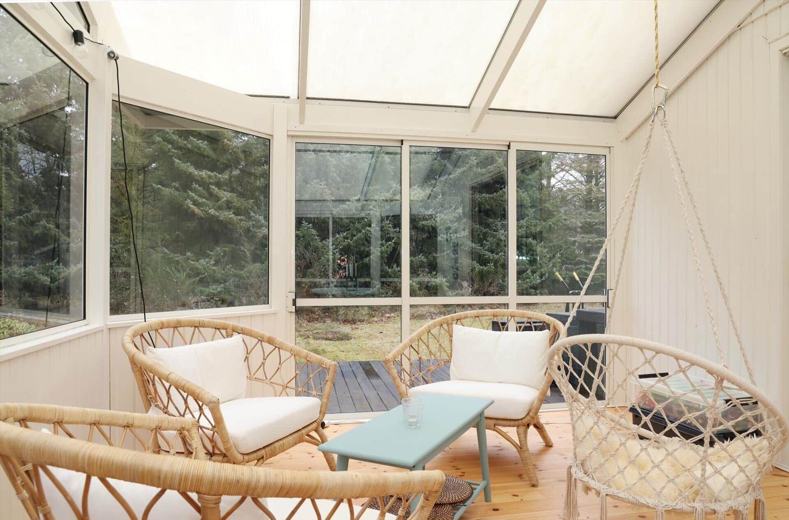 Terrace with rattan furniture and hanging chair. Glass walls and wooden floor.