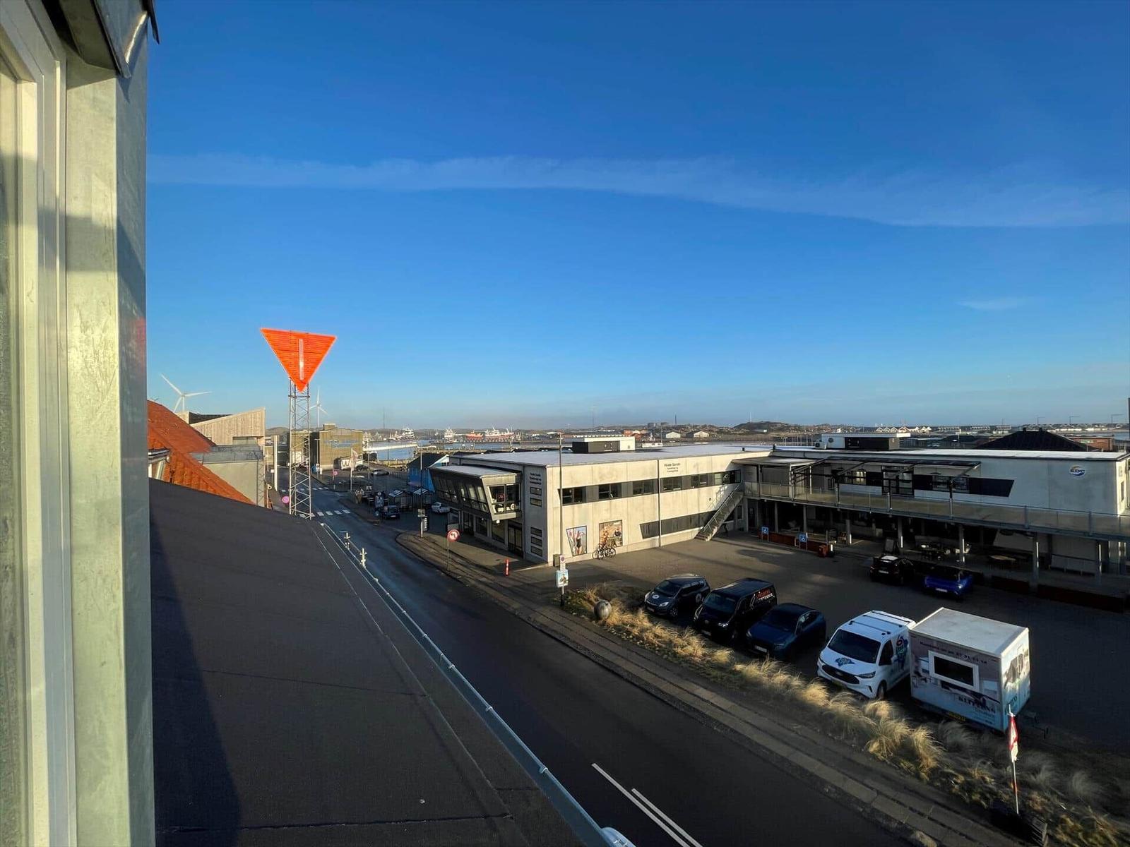 Ausblick auf Straße mit Parkplätzen und Industriegebäude unter blauem Himmel.