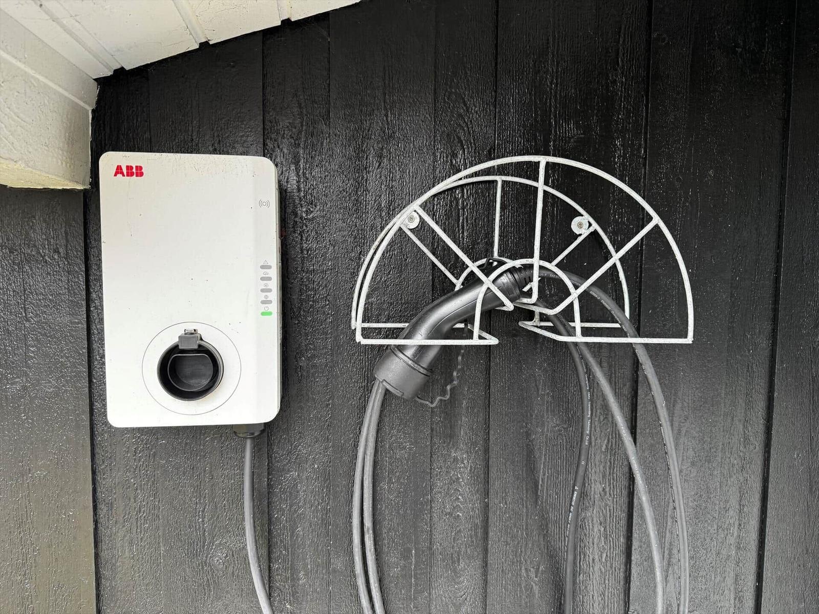 Elektrischer Ladepunkt mit Steckerhalter an schwarzer Holzwand.