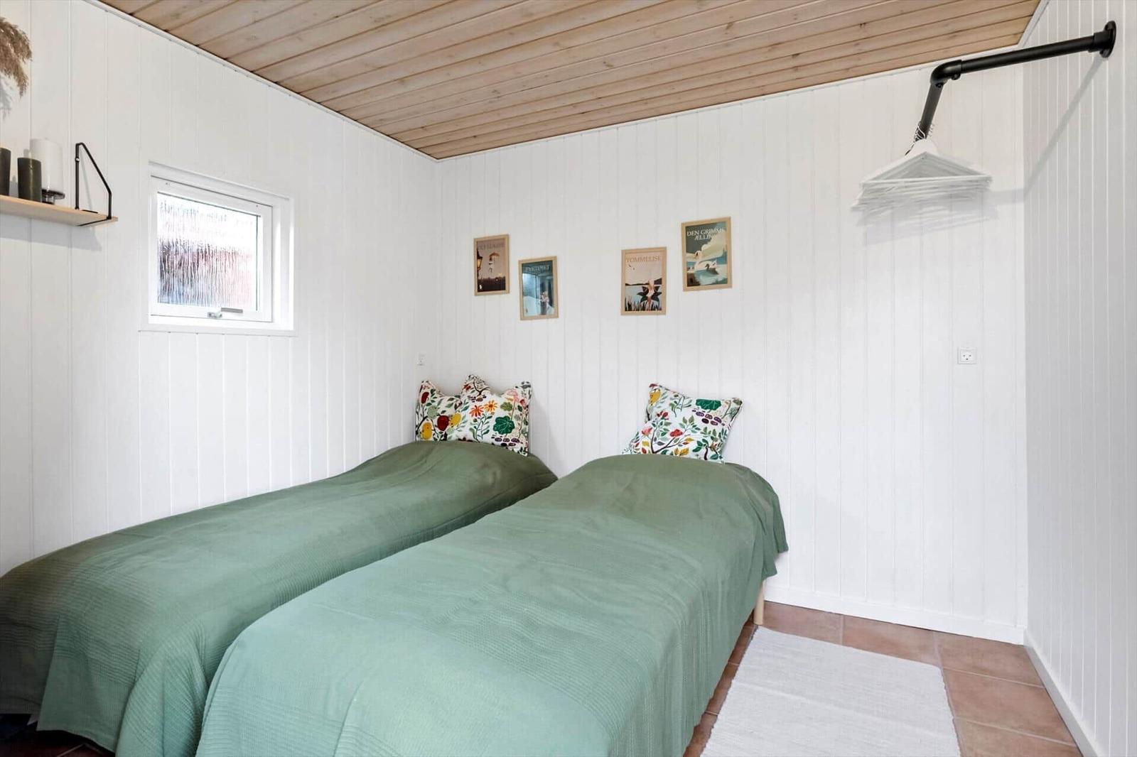 Two beds with green bedding and colorful pillows. White walls and wooden ceiling.