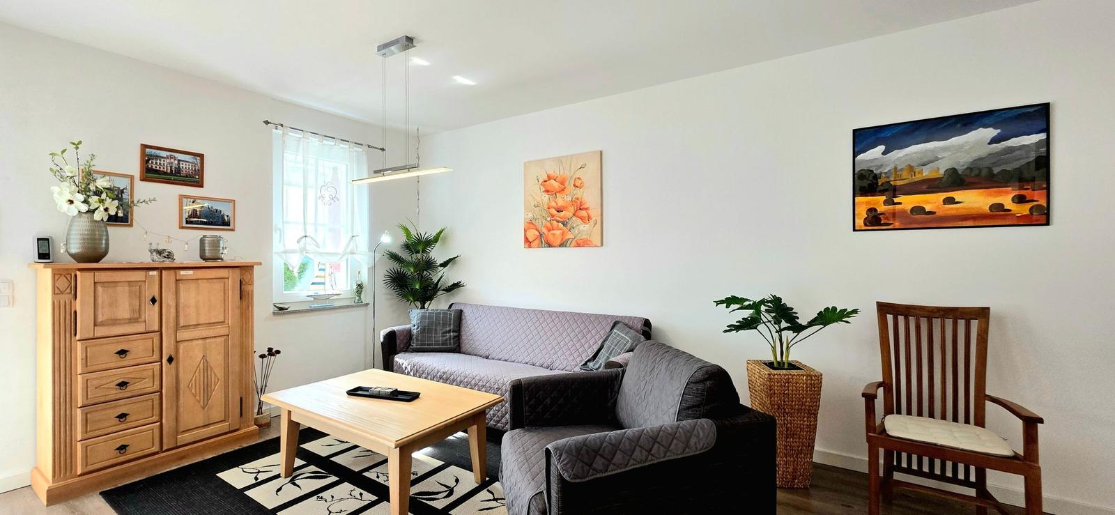 Wohnzimmer mit Sofa, Tisch und Wandbildern.