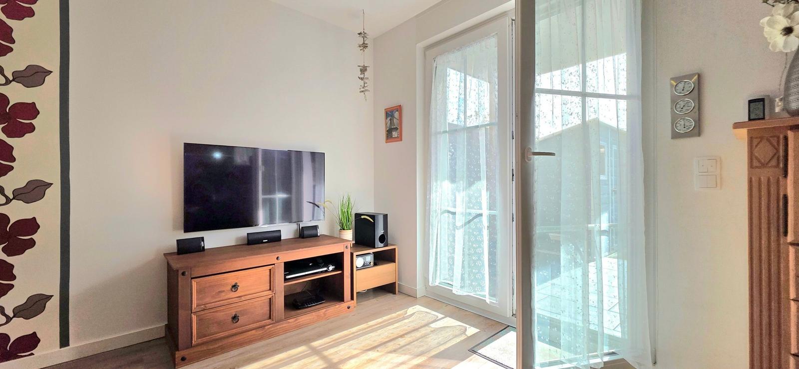 Wohnzimmer mit TV, Schrank und Glastür zum Balkon.