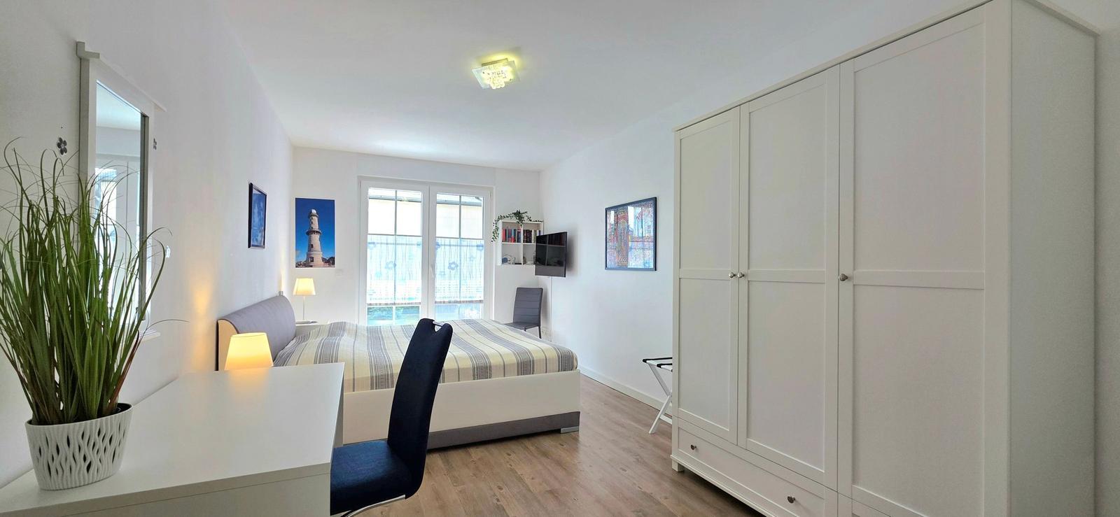 Schlafzimmer mit Bett, Schreibtisch, Kleiderschrank und Fenster.
