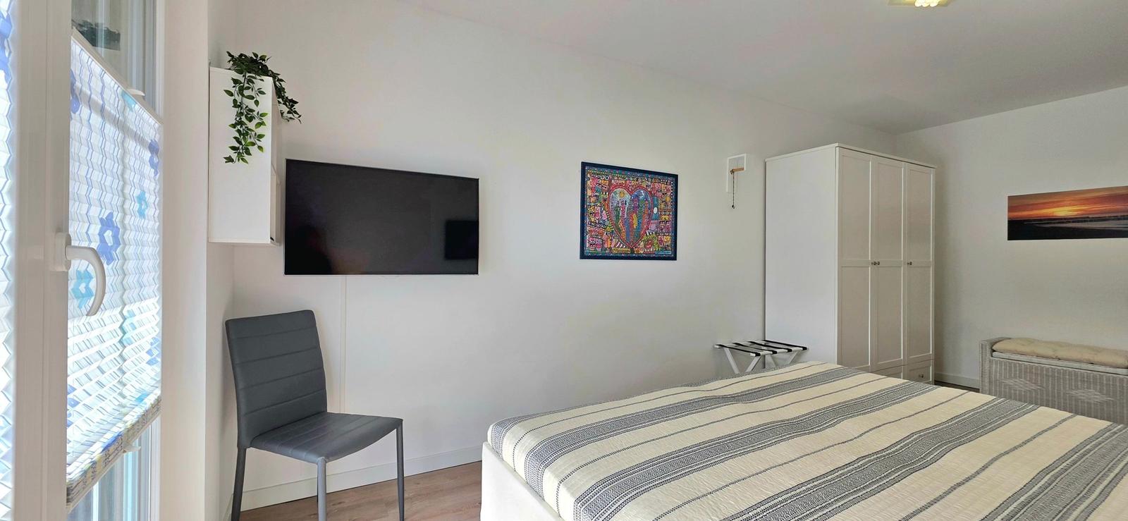 Schlafzimmer mit Bett, Fernseher, Kleiderschrank und Fenster