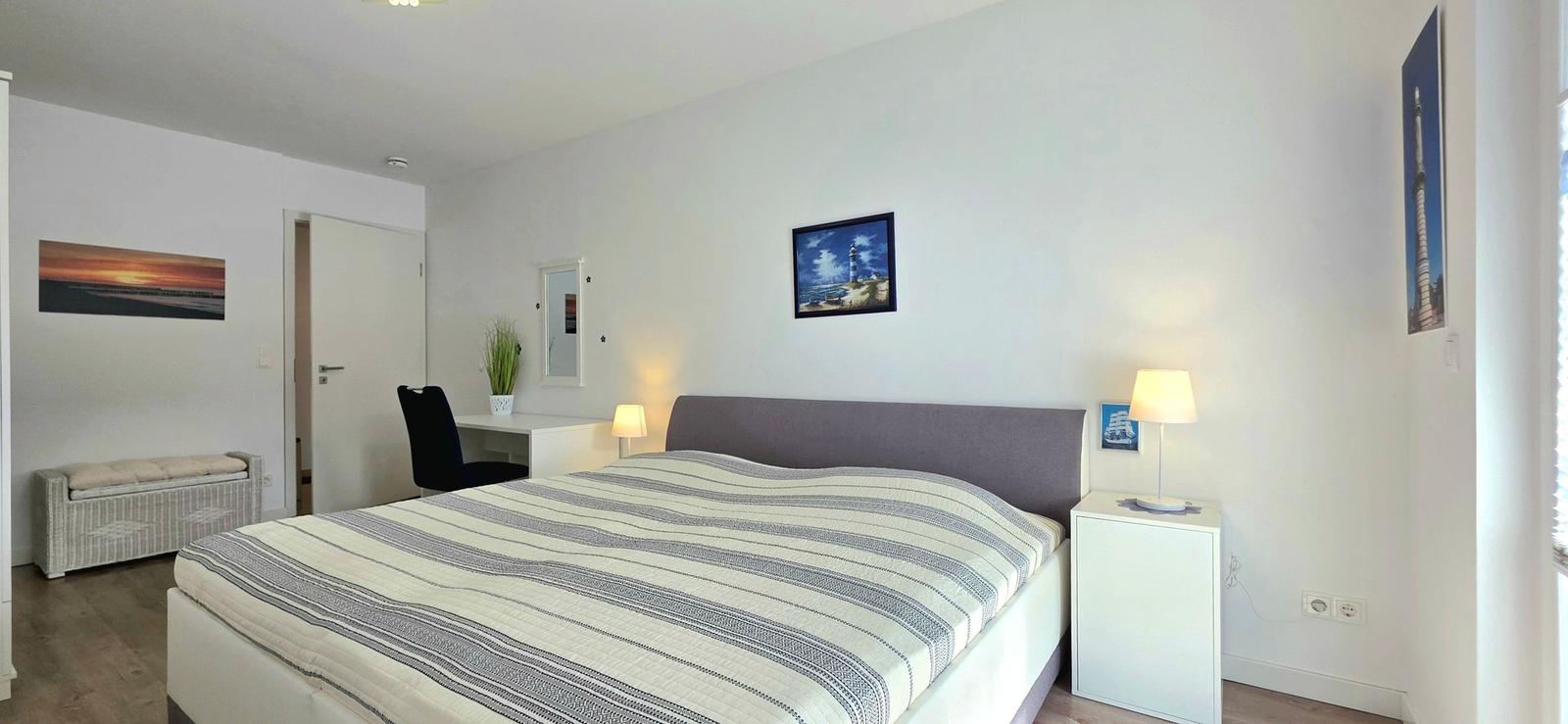 Schlafzimmer mit Bett, Nachttisch, Schreibtisch und Wandbildern.