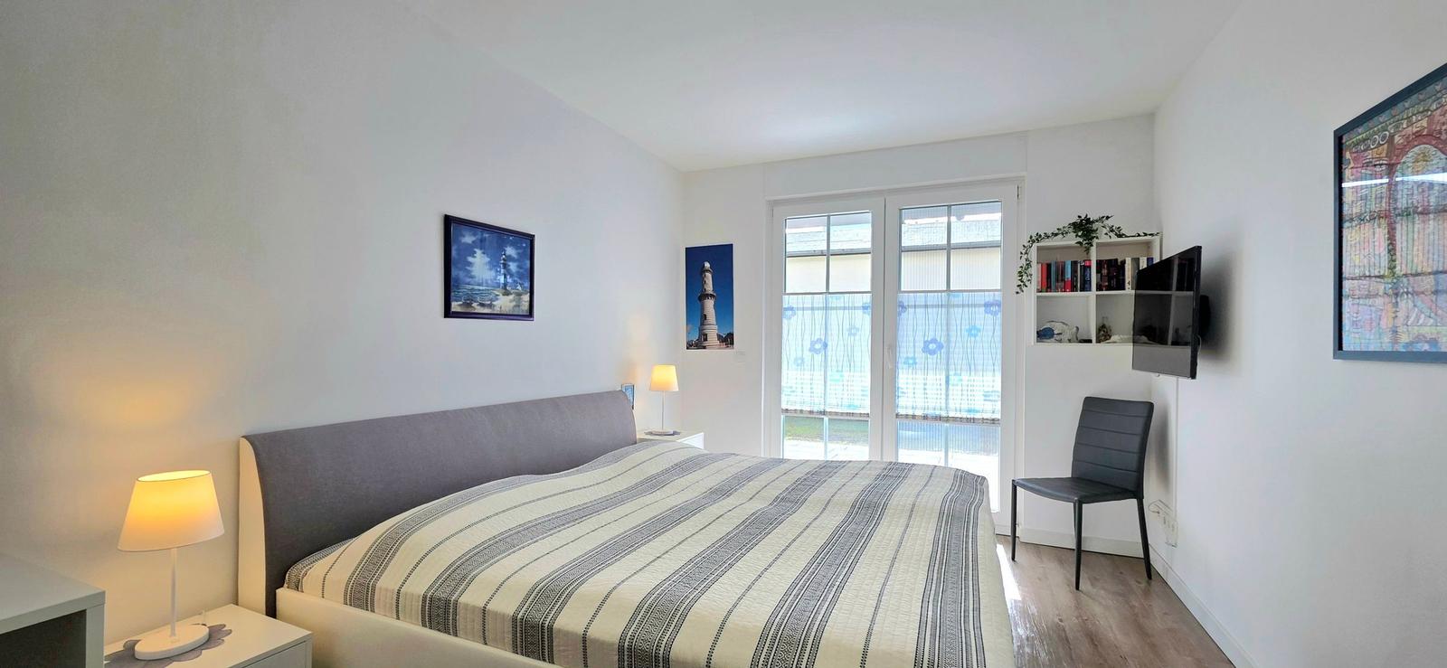 Schlafzimmer mit Bett, TV, Stuhl und Fenster zur Aussicht.