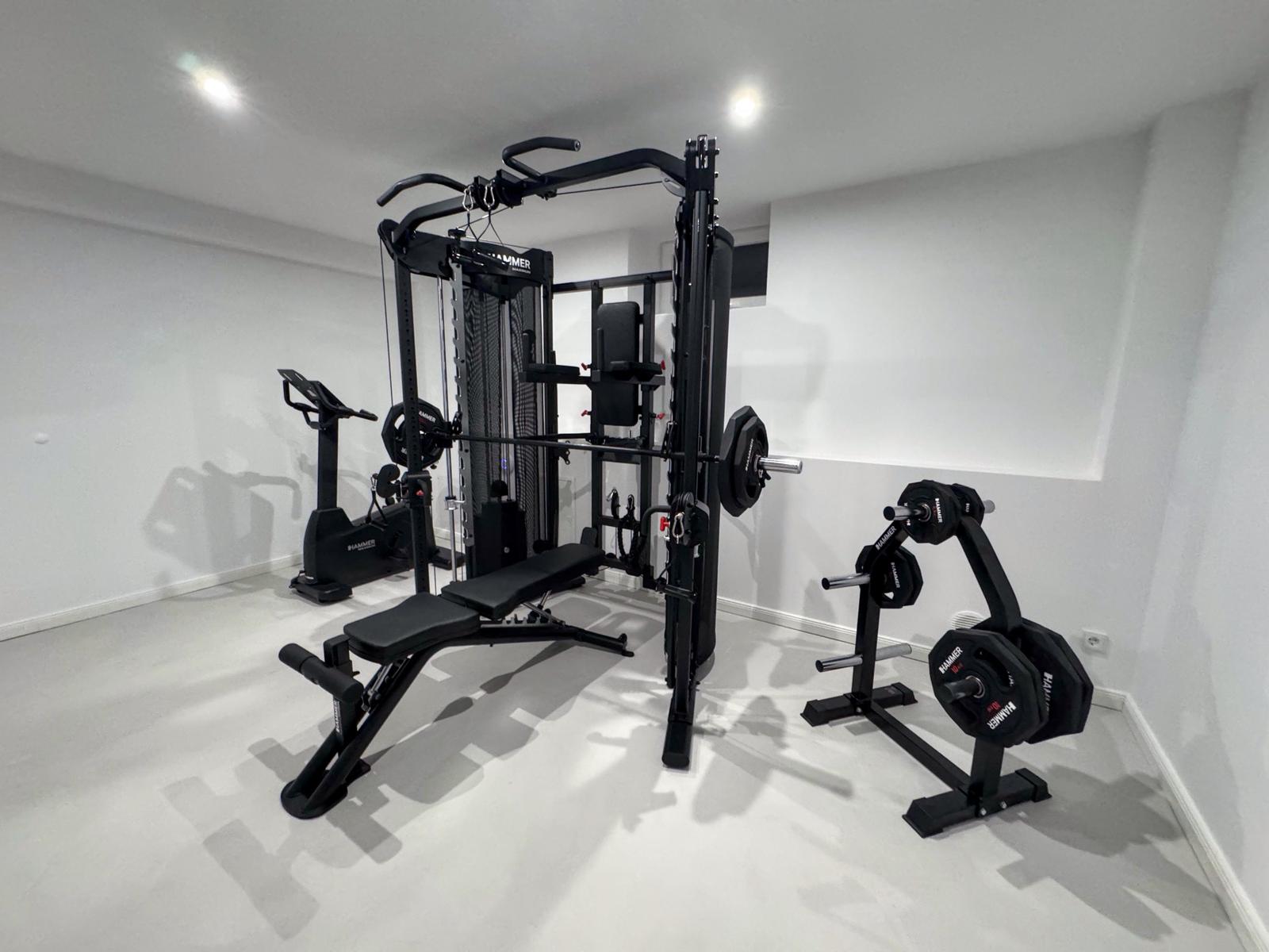 Fitnessraum mit Kraftstation, Bank und Hantelständer.