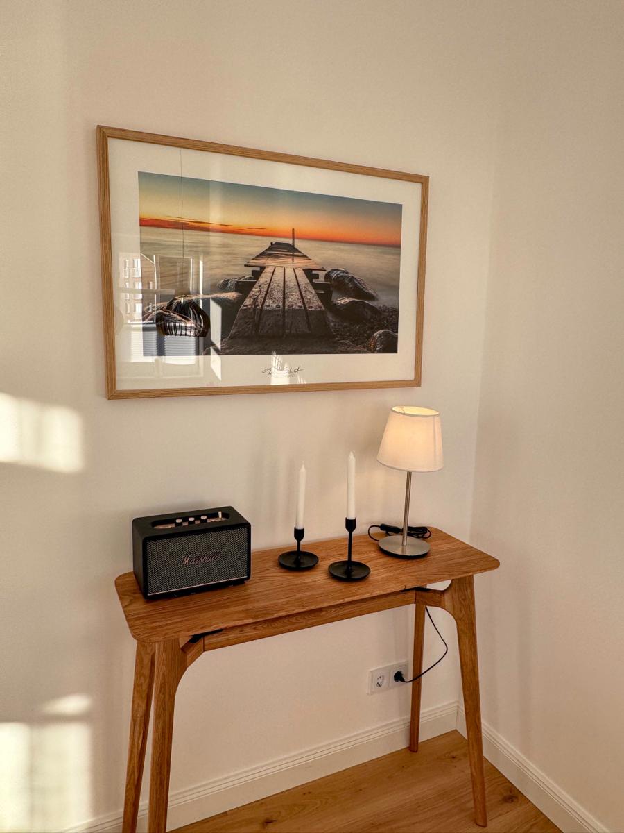 Holztisch mit Lampe, Kerzen und Lautsprecher unter einem Bild an der Wand.