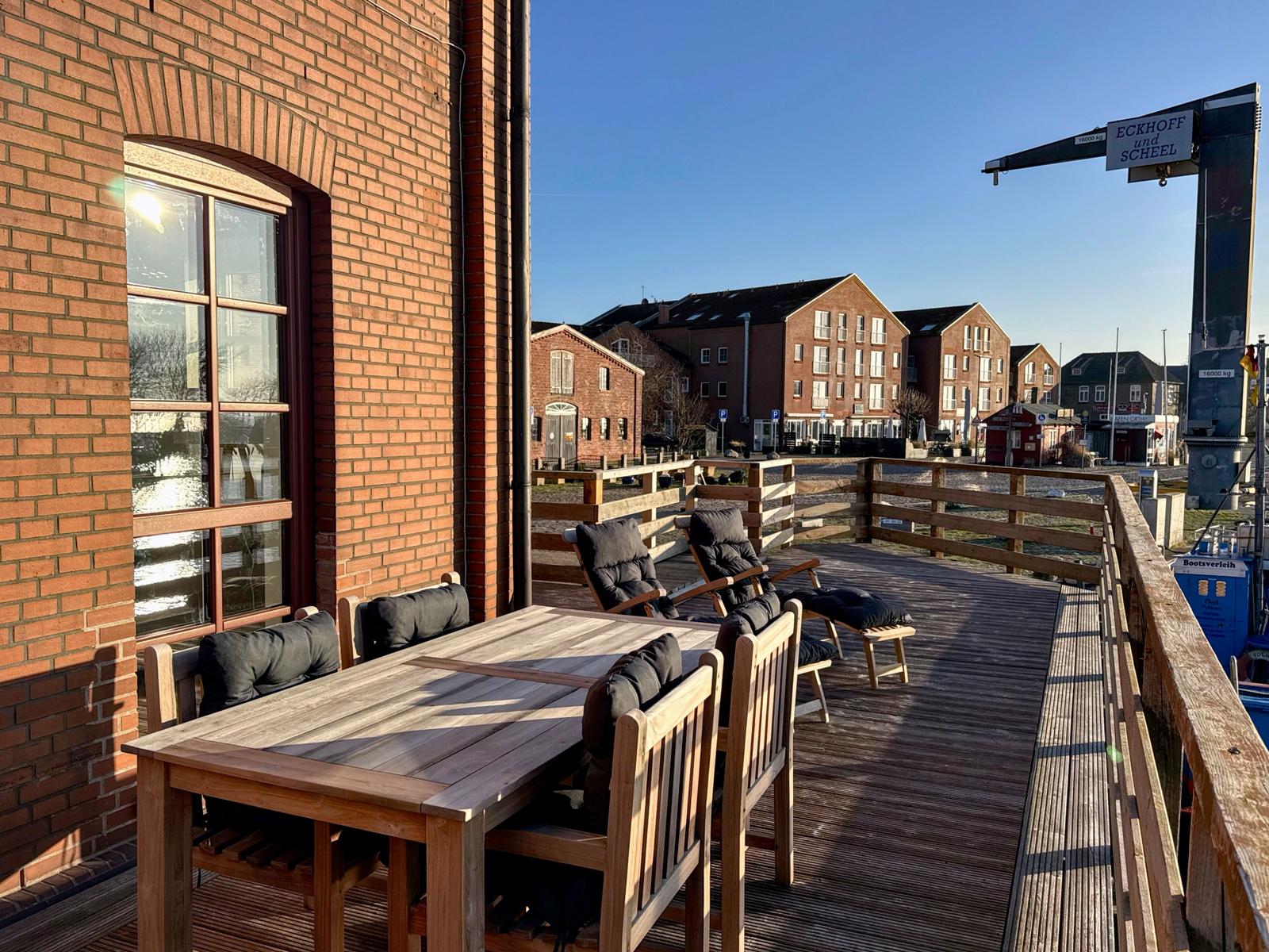 Terrasse mit Holztisch und Stühlen, Blick auf Gebäude und Krane.