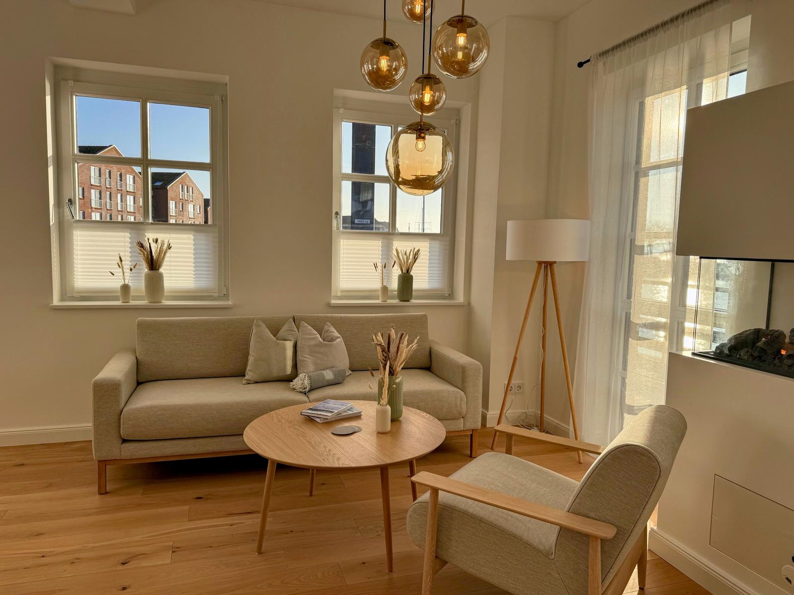 Wohnzimmer mit Sofa, Sessel und runden Tisch. Fenster und Hängelampen.