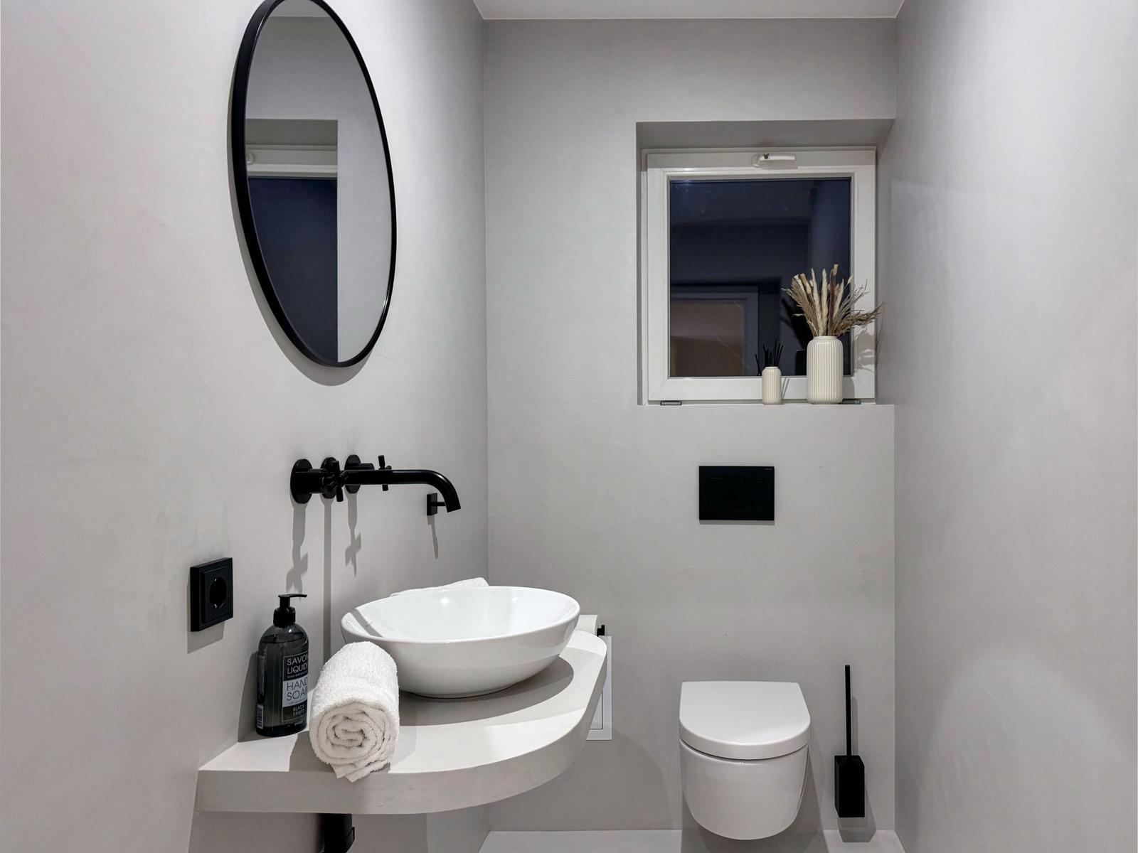 Badezimmer mit Waschbecken, Spiegel und Toilette.