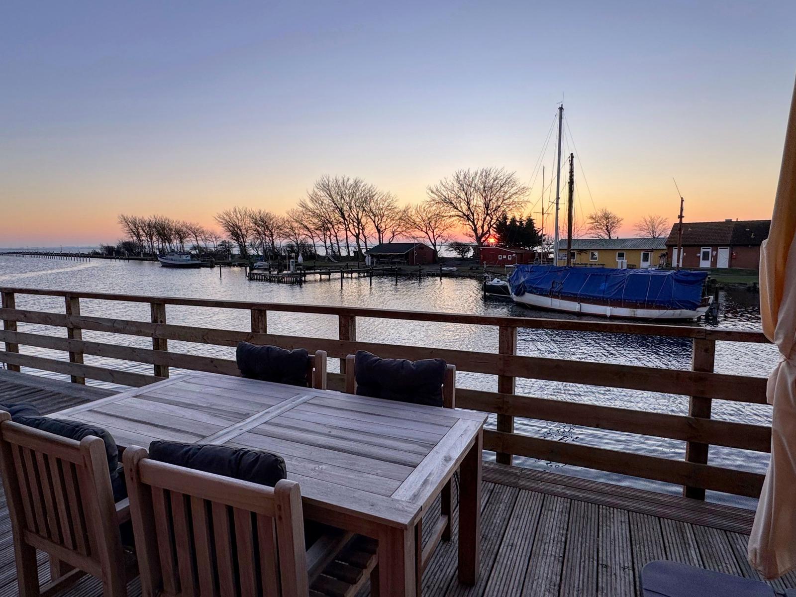 Terrasse mit Tisch und Stühlen über Wasserblick zum Sonnenuntergang.