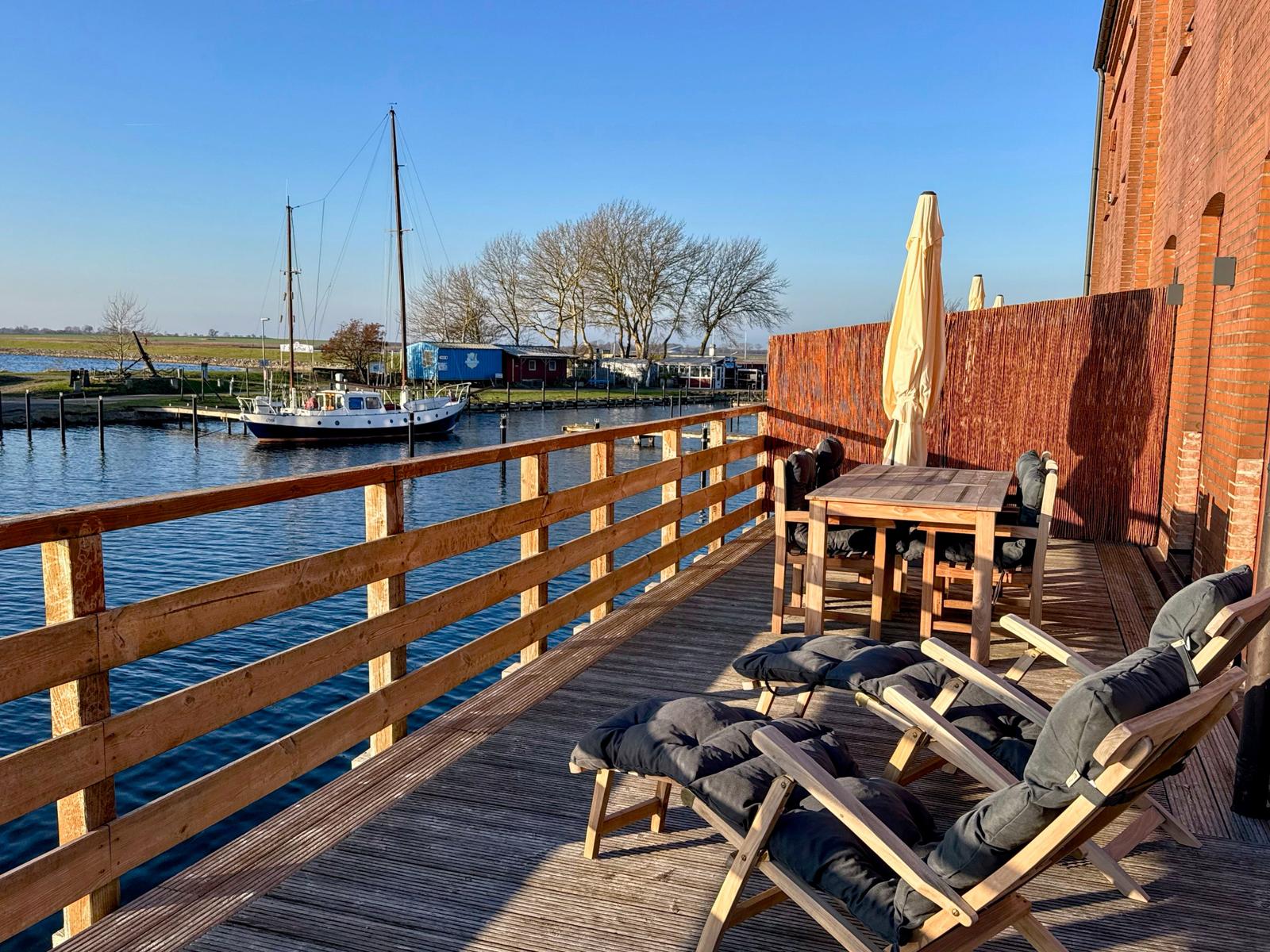 Holzterrasse mit Liegestühlen und Tisch am Wasser mit Boot.
