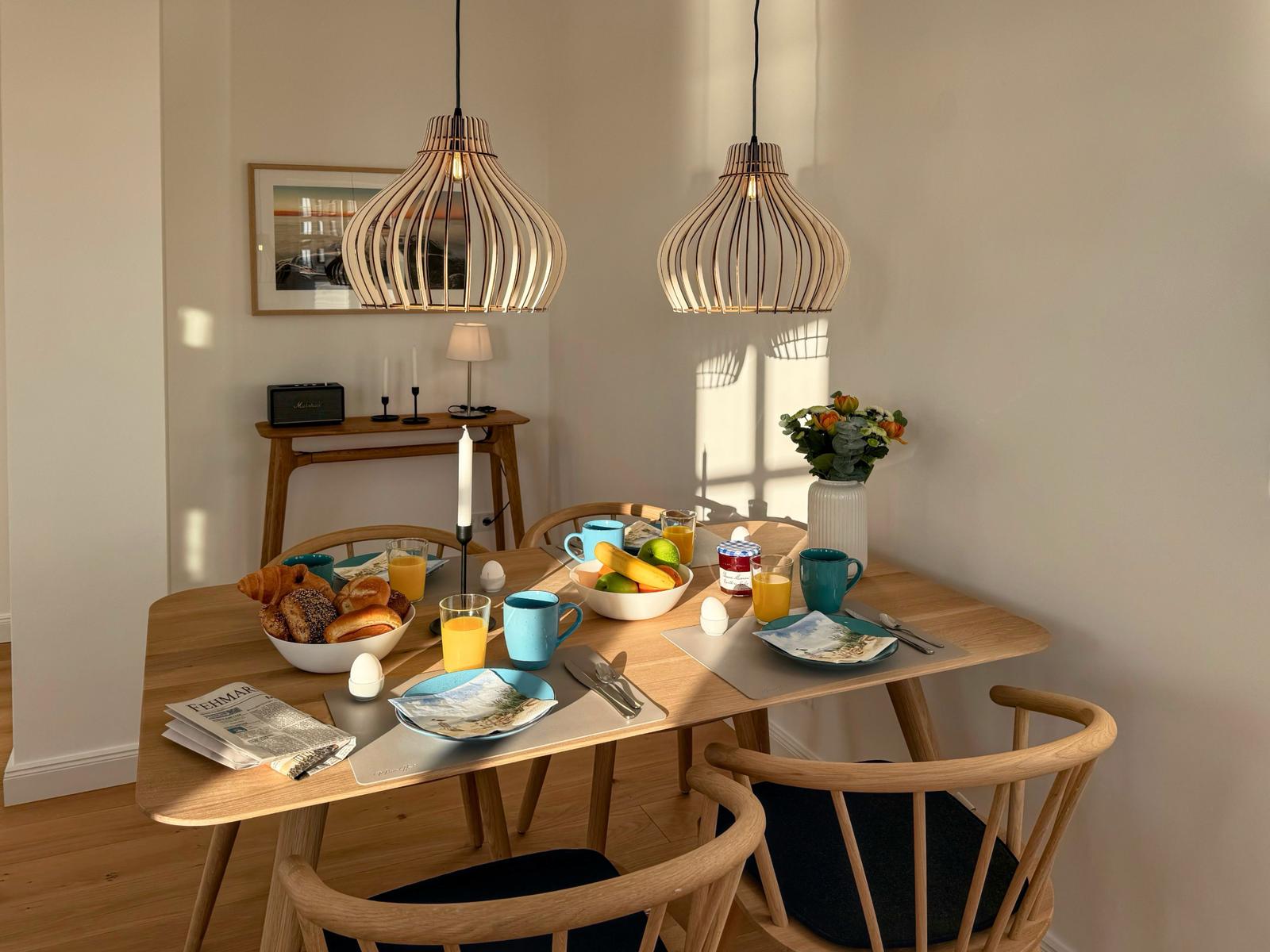 Esstisch mit vier Stühlen, zwei Hängelampen und Frühstücksausstattung.
