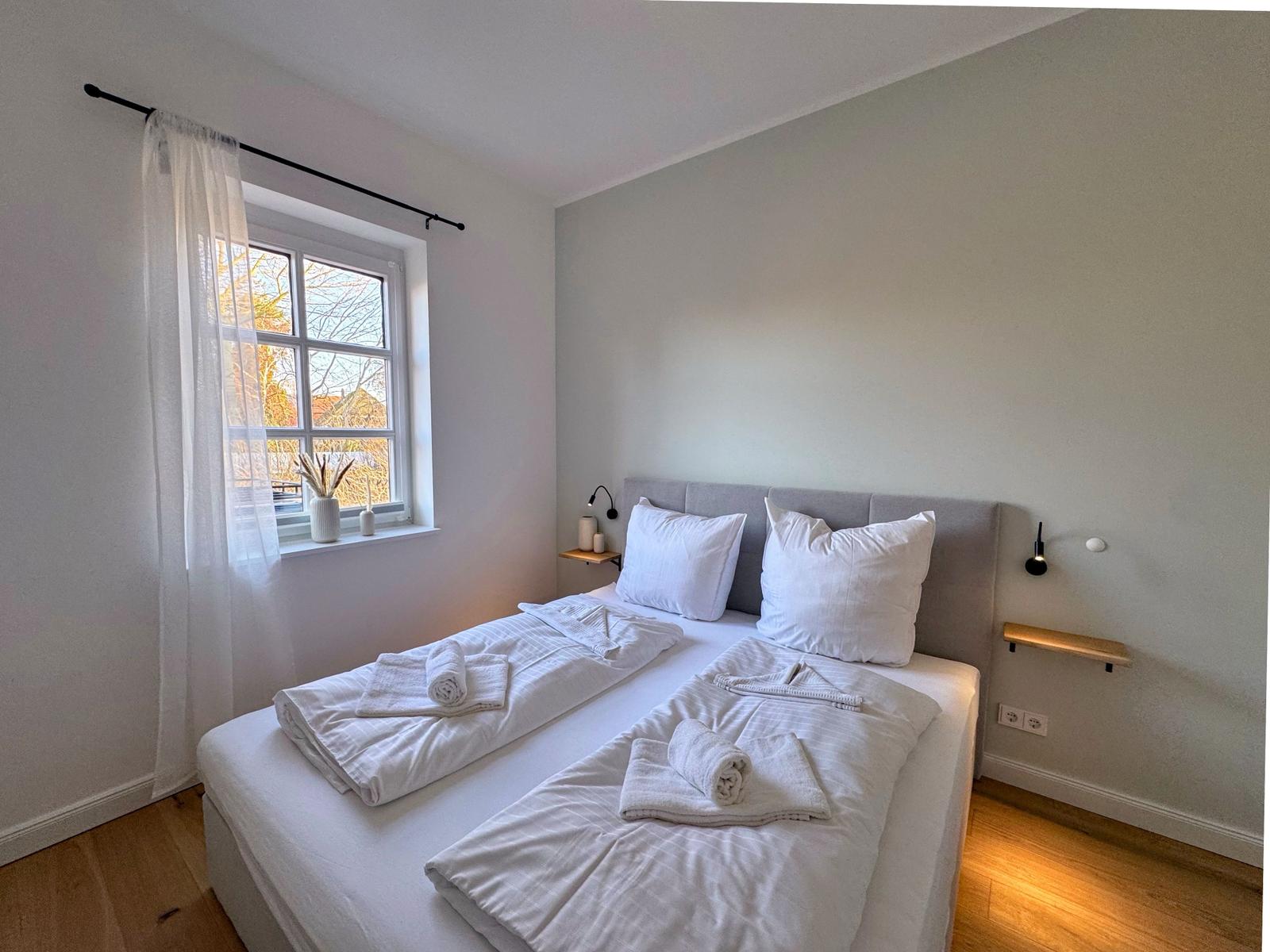 Schlafzimmer mit Doppelbett, Fenster und Holzboden.