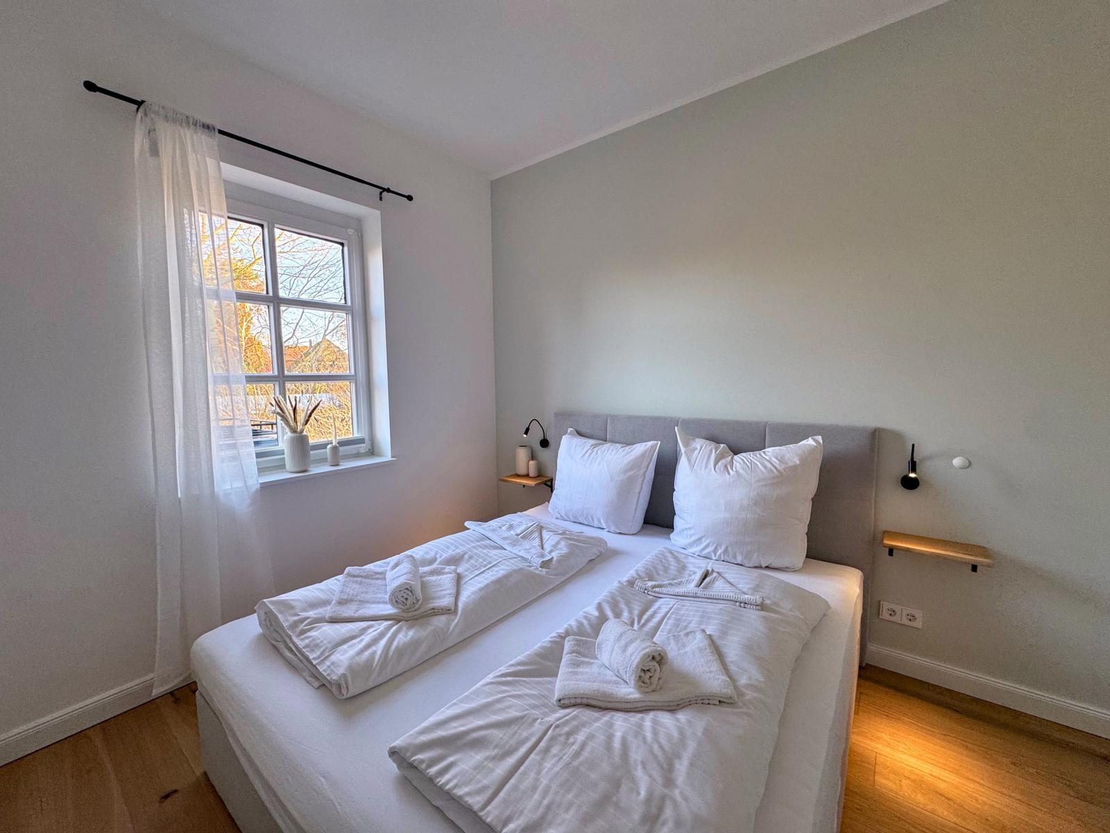 Schlafzimmer mit Doppelbett, Fenster und Holzboden.