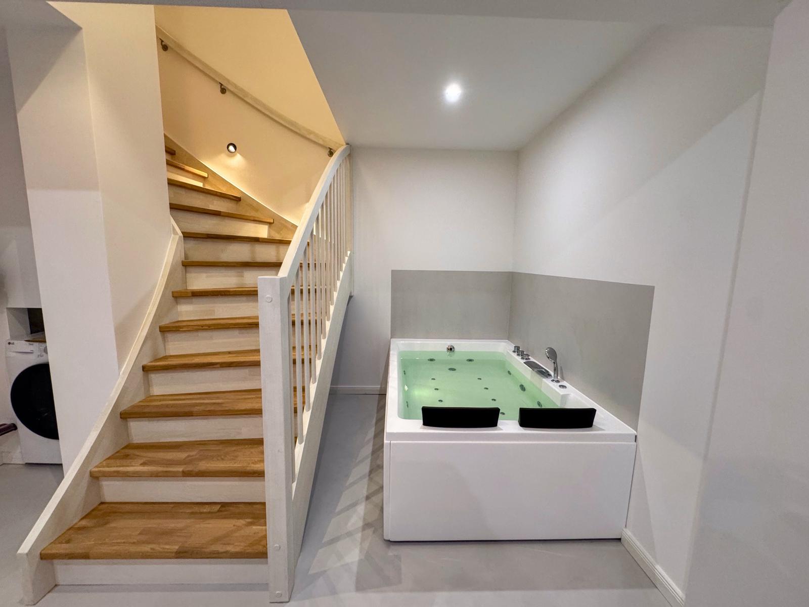 Eine Whirlpool-Badewanne neben einer Treppe mit Holzstufen und weißem Geländer.