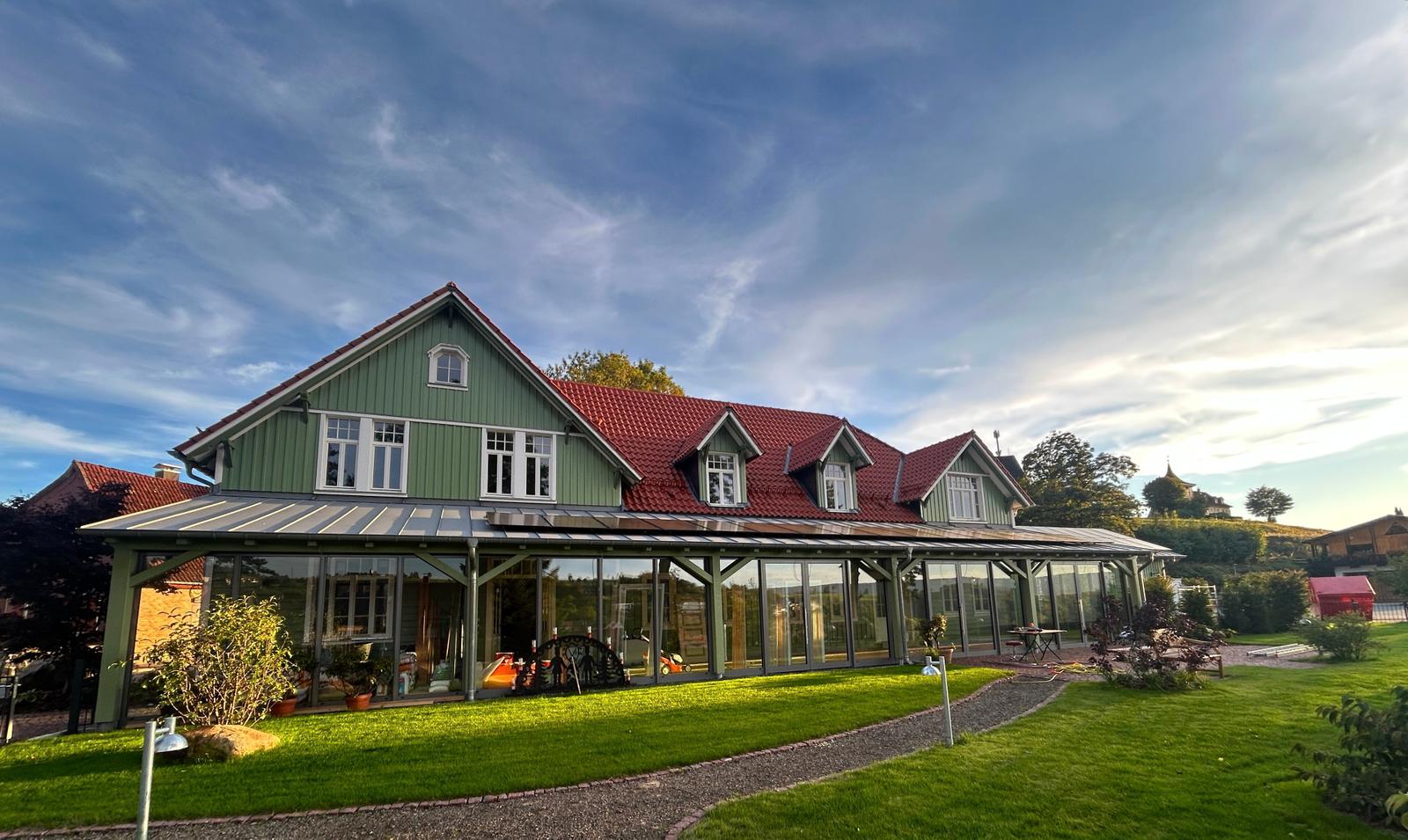 Grünes Haus mit rotem Dach und großem Glasbereich im Garten