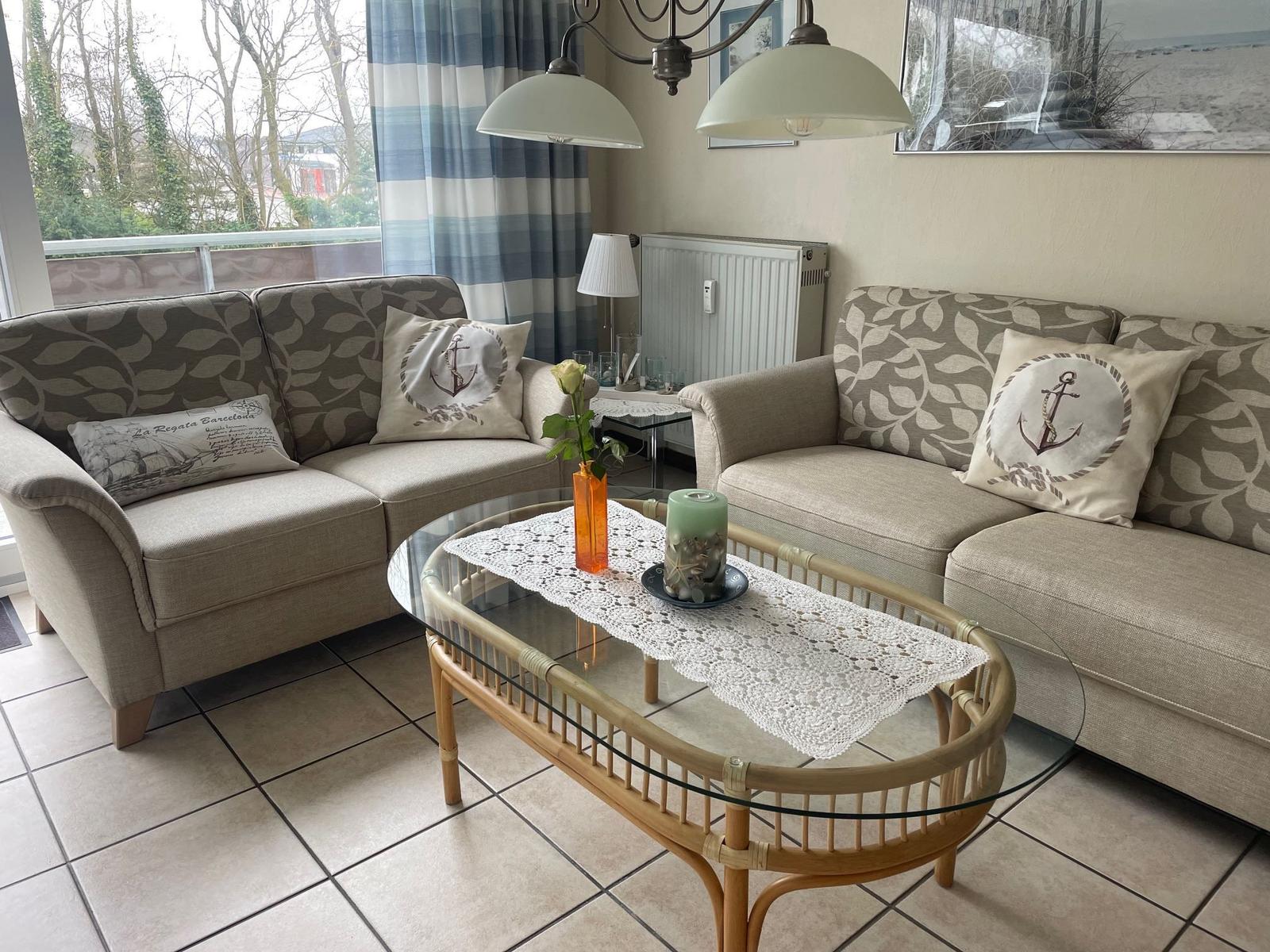 Wohnzimmer mit zwei Sofas, Glas-Tisch und Blick auf Balkon.