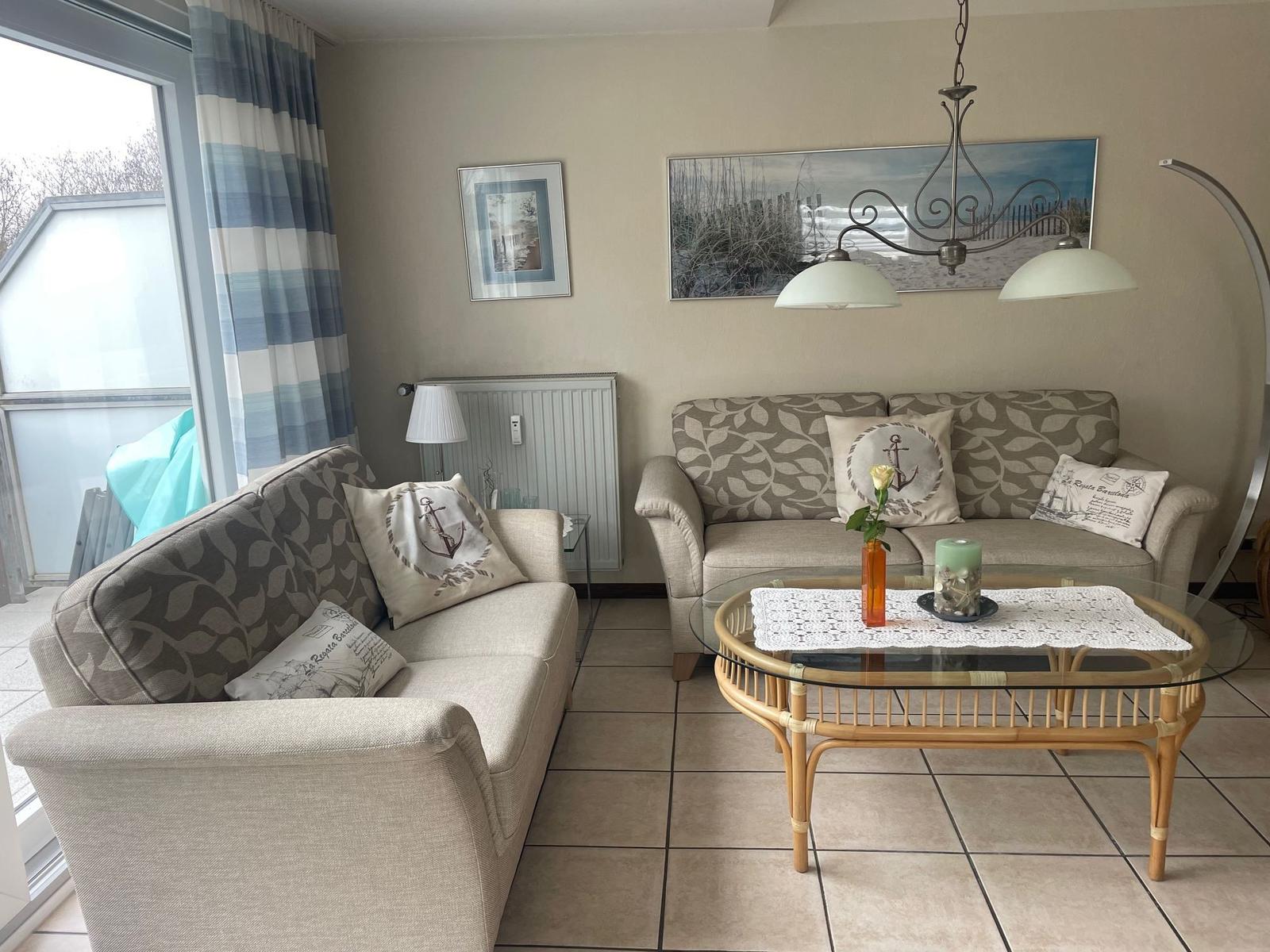 Wohnzimmer mit zwei Sofas, Glas-Tisch und Wandbildern.