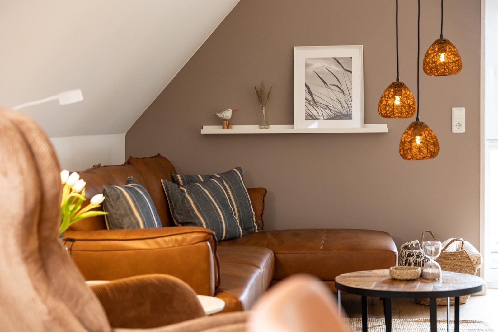 Ein Wohnzimmer mit braunem Ledersofa, hängenden Lampen und einem Tisch.