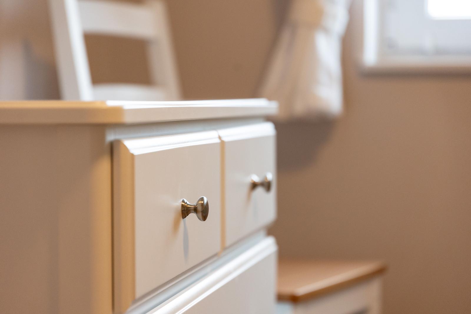 Weißer Schrank mit zwei Schubladen und Metallgriffen in einem Raum.