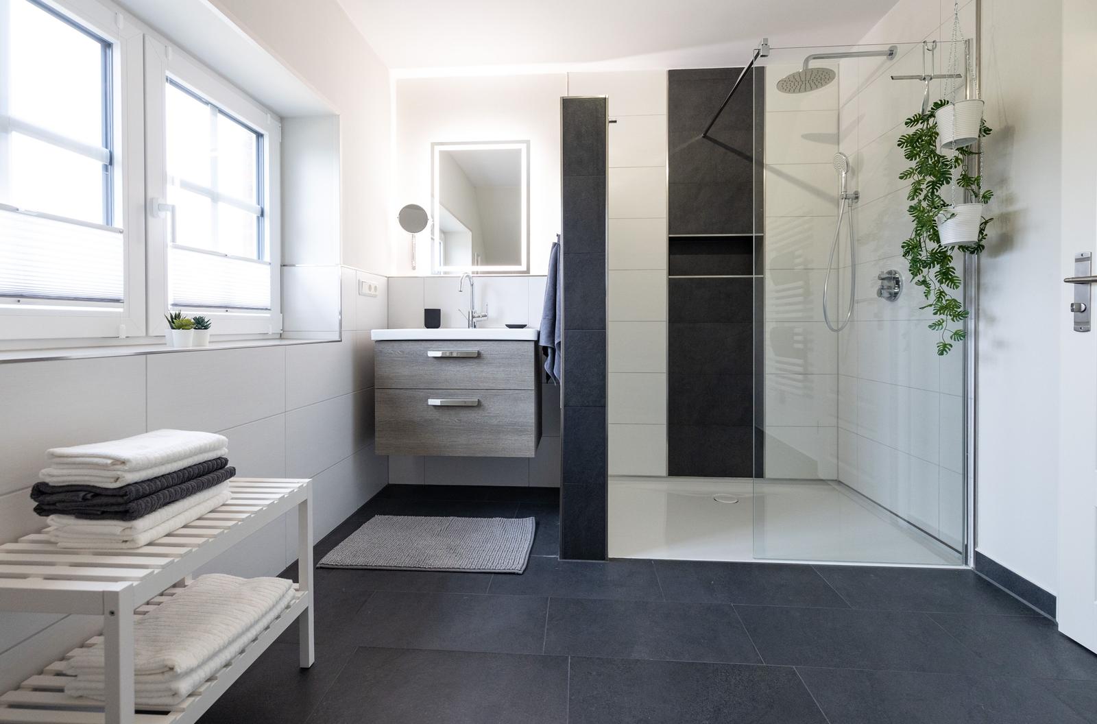 Badezimmer mit Dusche, Waschbecken und Fenster. Handtuchständer und Pflanzen sind sichtbar.