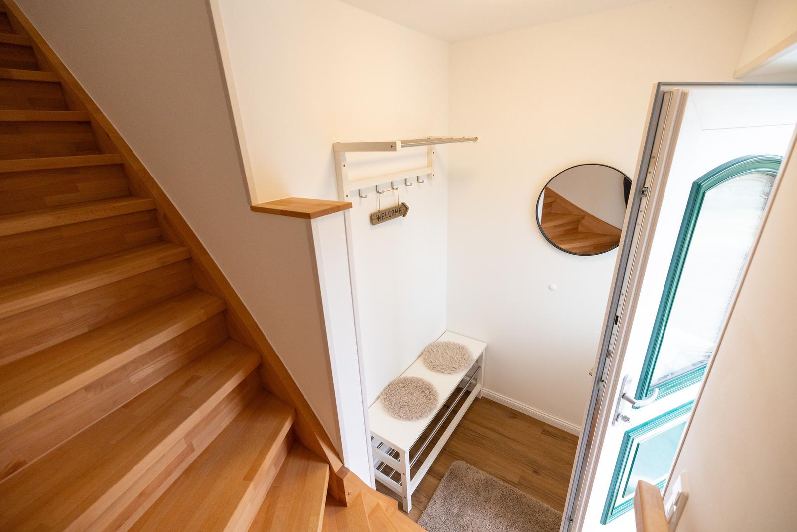 Eingangsbereich mit Holztreppe, Kleiderständer und runder Wandspiegel.