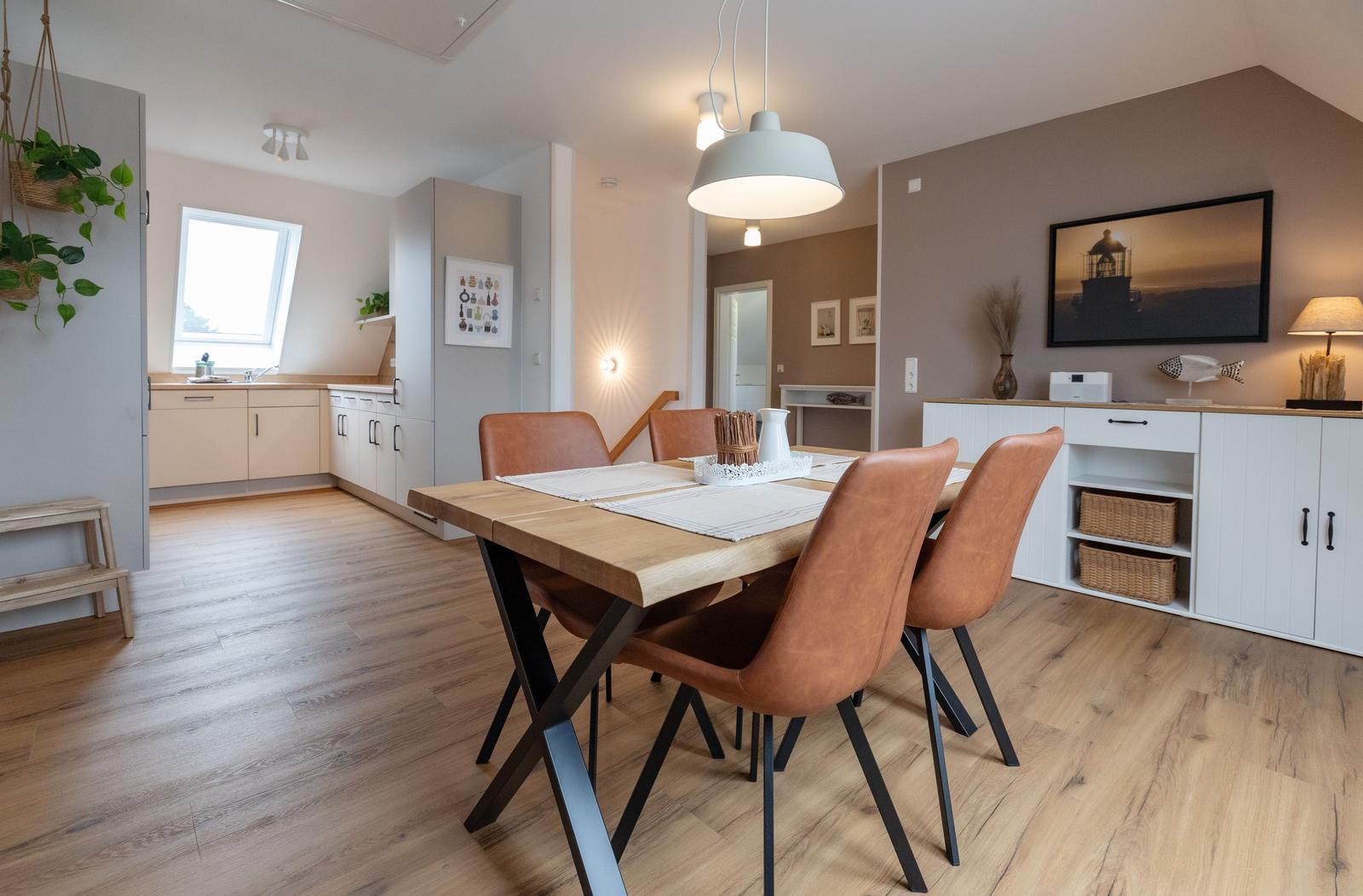 Esszimmer mit Holztisch und braunen Stühlen. Küche und Wohnbereich im Hintergrund.