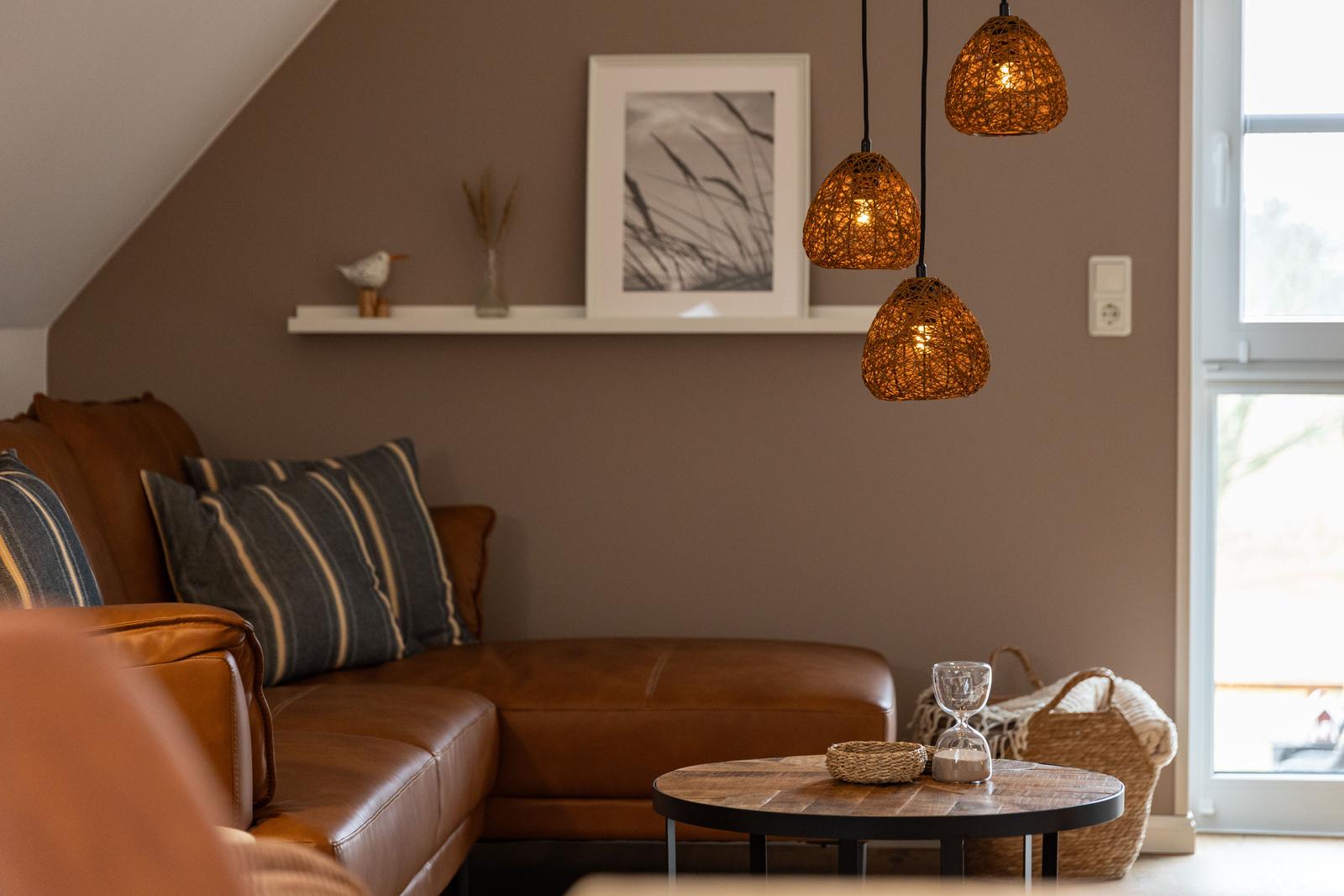 Wohnzimmer mit Ledersofa, runden Tisch und drei hängenden Lampen.