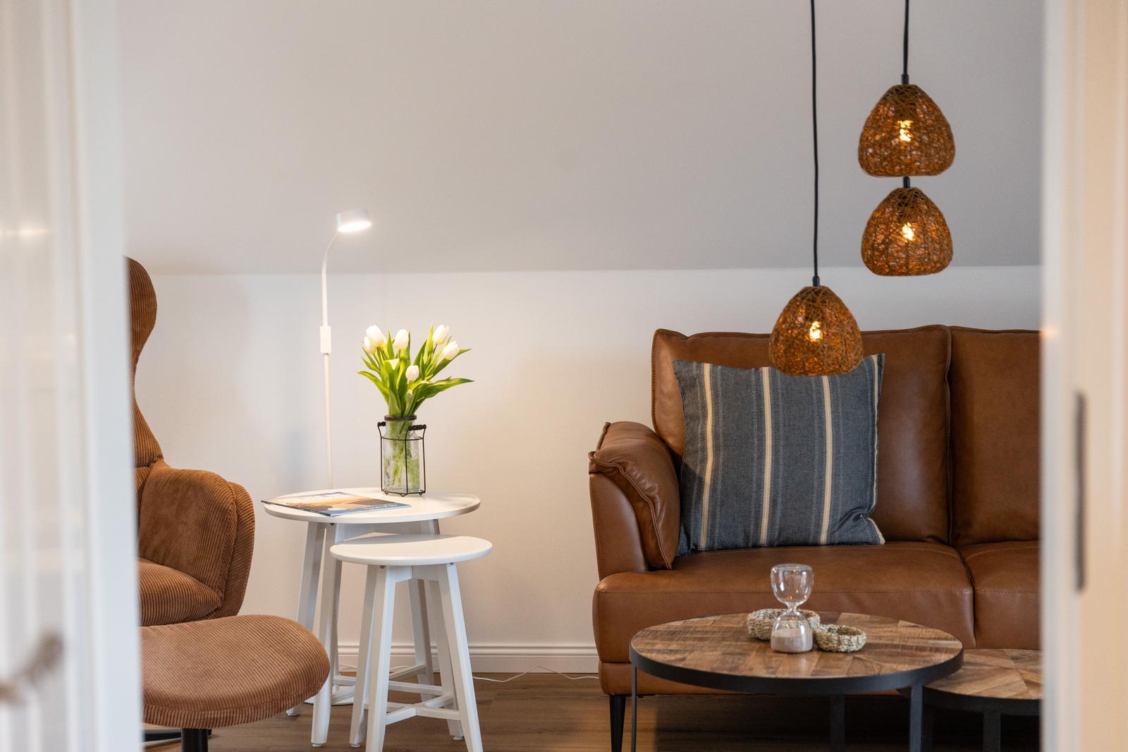 Ein Wohnbereich mit braunem Sofa, weißen Tischen und hängenden Lampen.