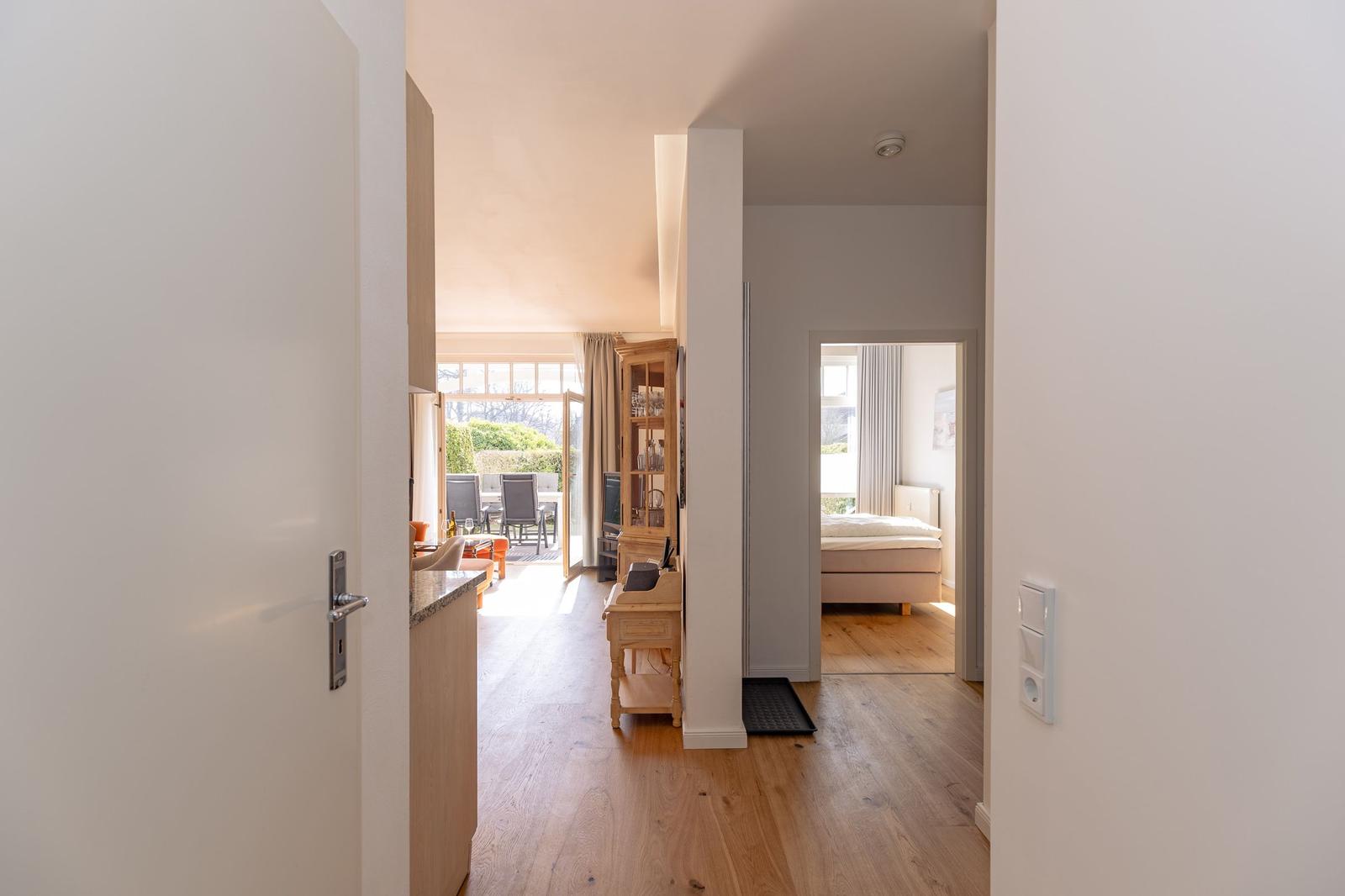 Zimmer mit Doppelbett, Sessel und Holzboden. Fenster mit Vorhängen.