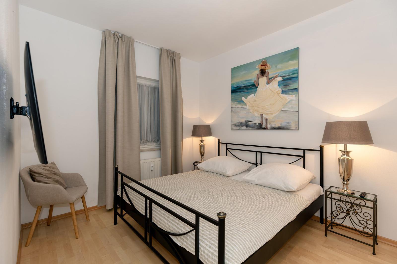 Ein Schlafzimmer mit Doppelbett, Stuhl und Fenster mit Vorhängen.