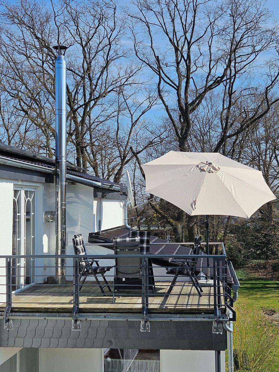 Terrasse mit Sonnenschirm und Sitzgelegenheiten. Hintergrund: Bäume und Haus.