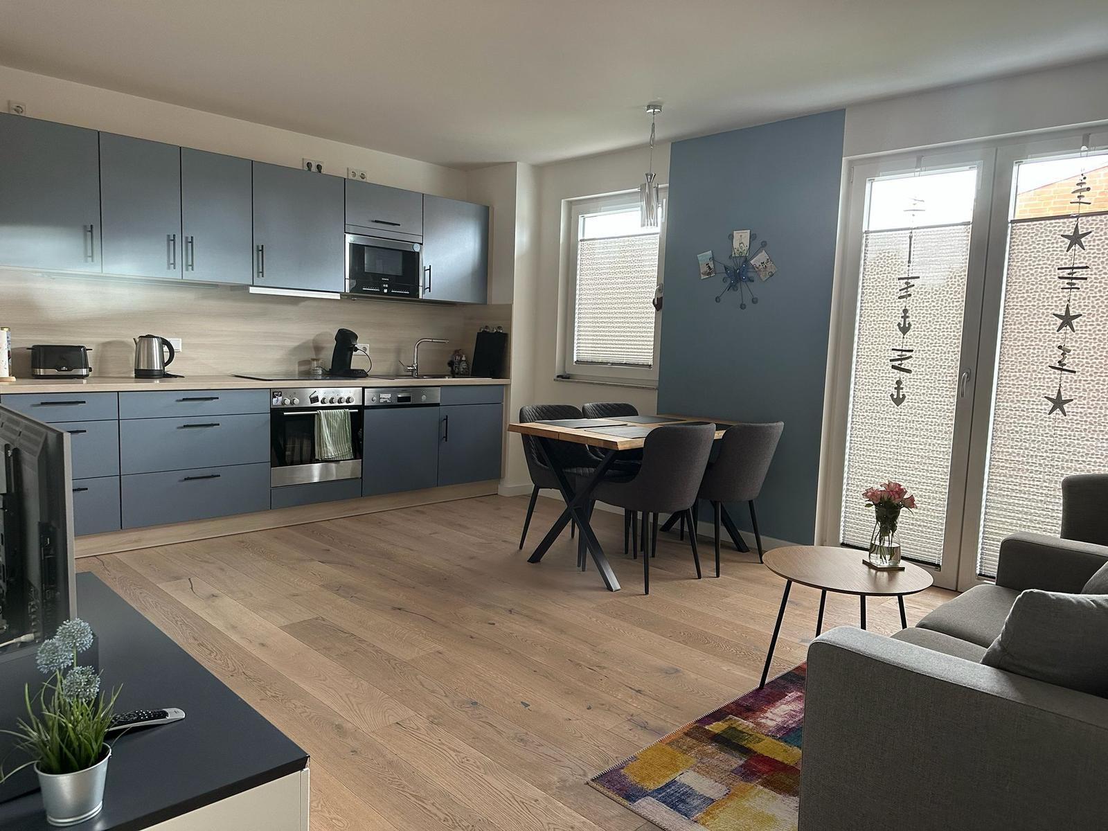 Küche mit Essbereich und Wohnzimmer mit Holzboden und grauer Einbauküche.