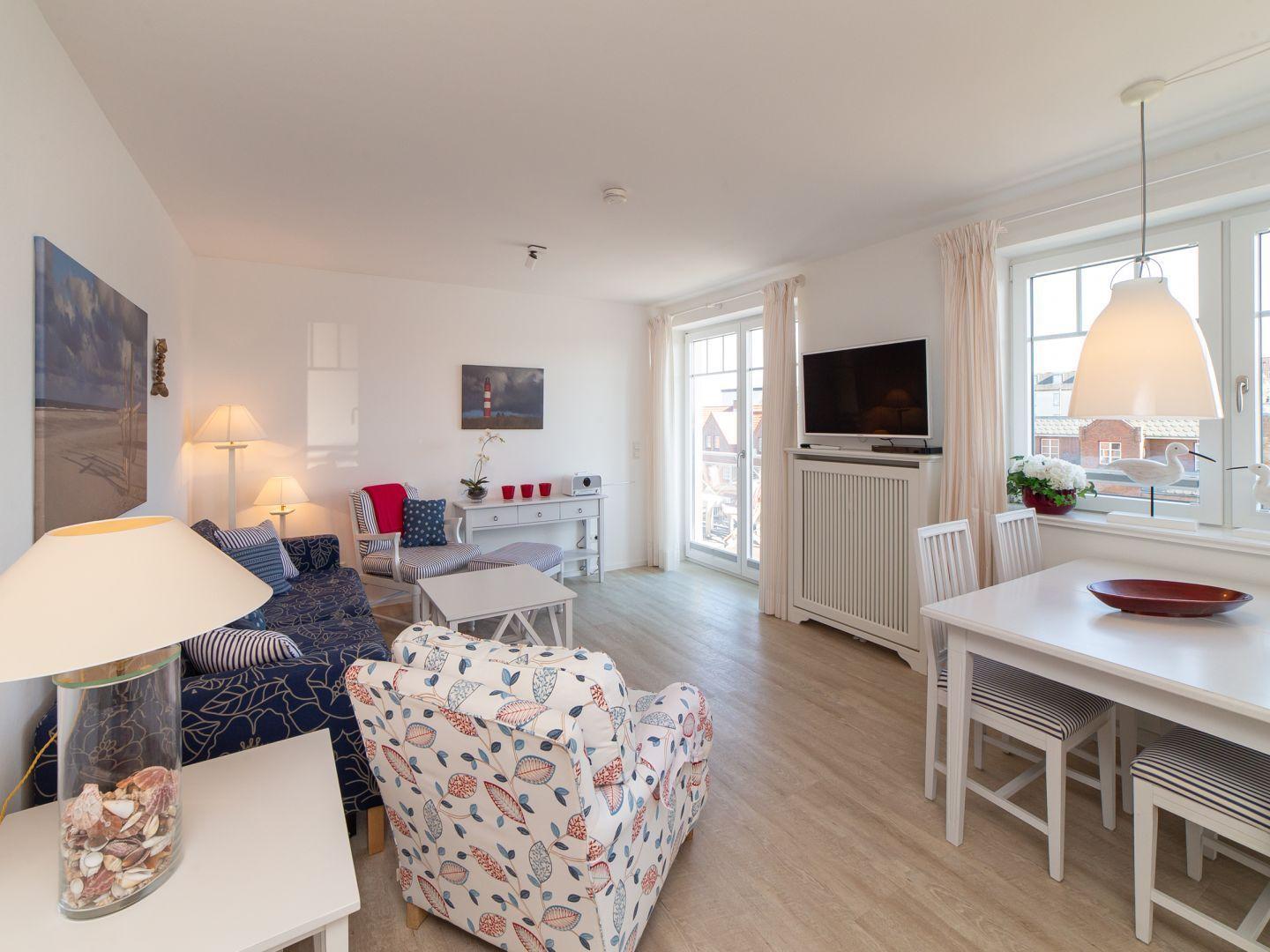Wohn- und Essbereich mit Sofa, Stühlen und Fernseher. Fenster mit Blick auf die Straße.