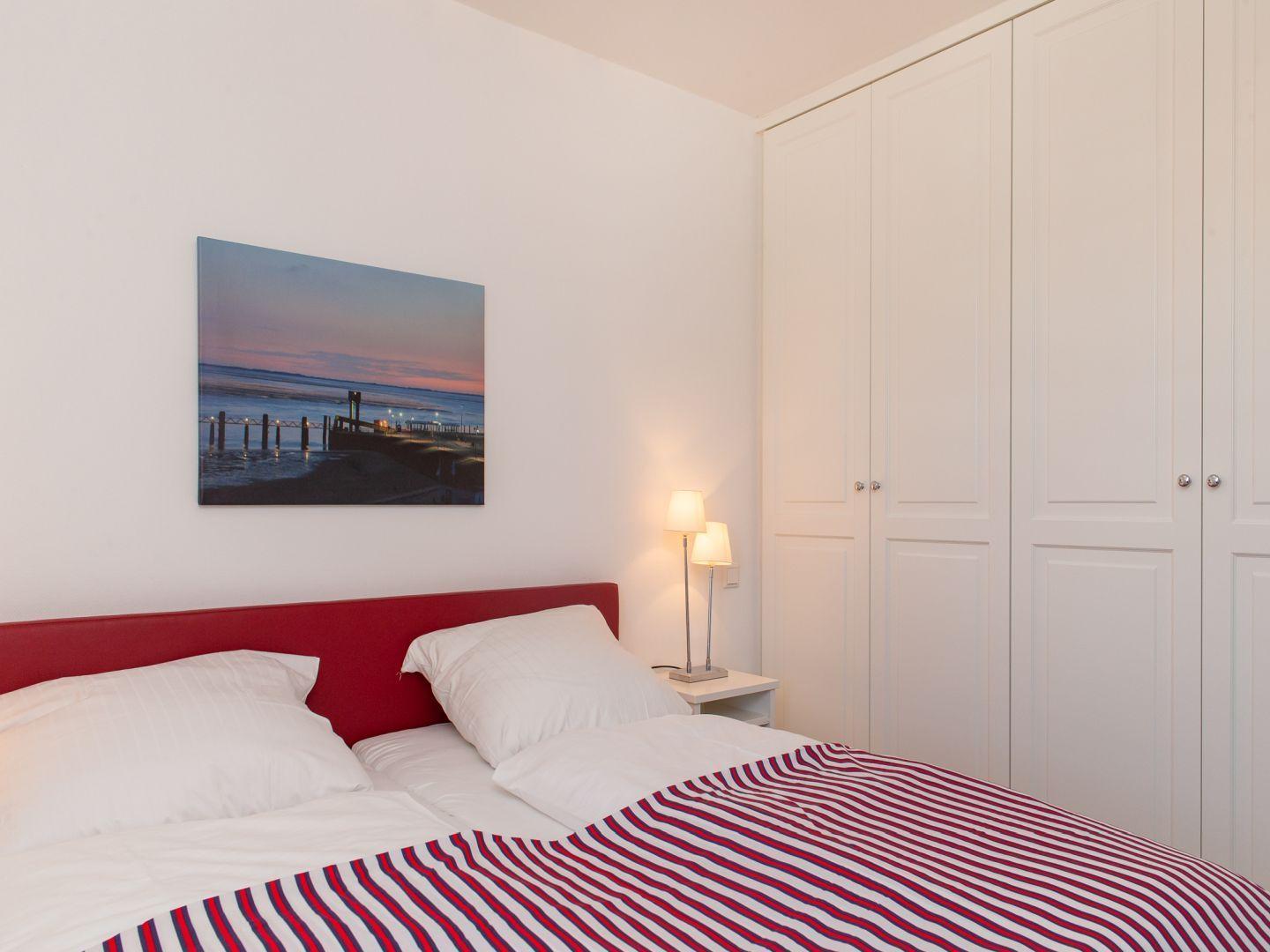 Schlafzimmer mit rotem Bett, weißen Wänden und Kleiderschrank.