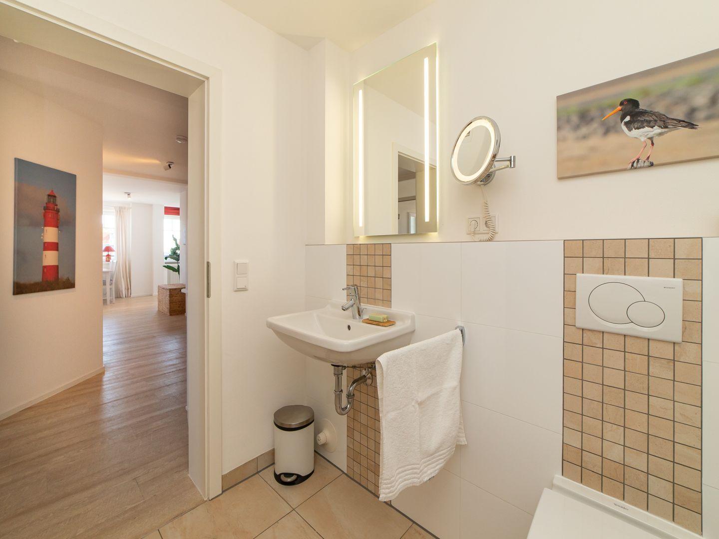 Badezimmer mit Waschbecken, Spiegel und Wandbildern.