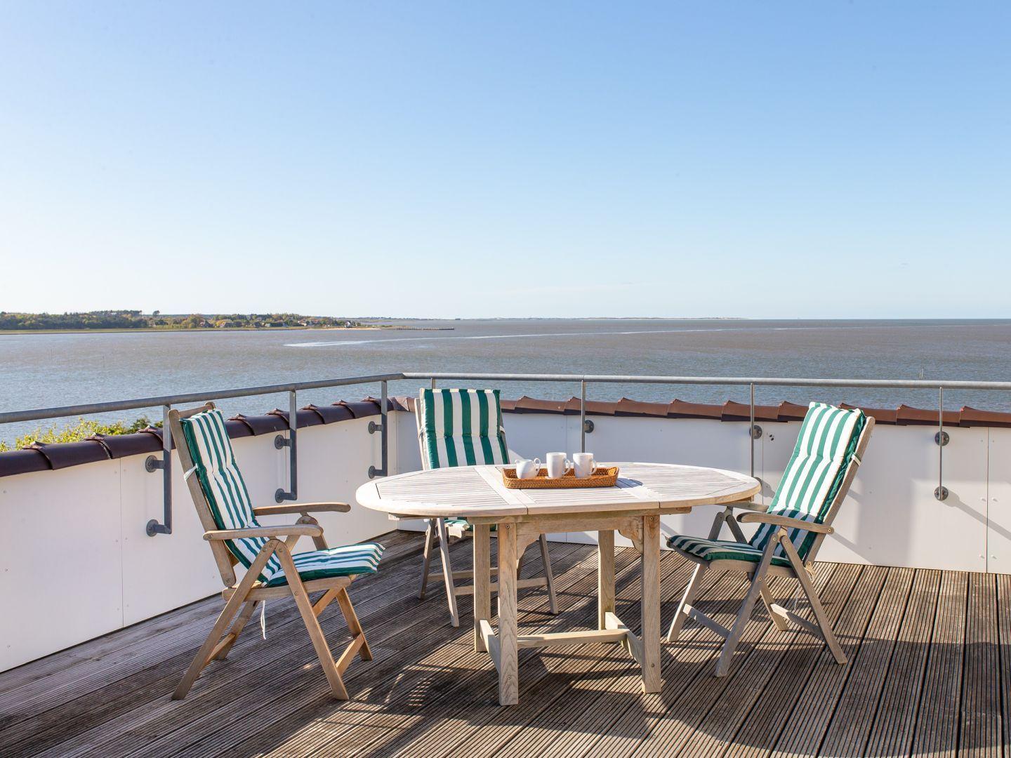 Terrasse mit Tisch und Stühlen, Blick auf Wasser und Horizont.