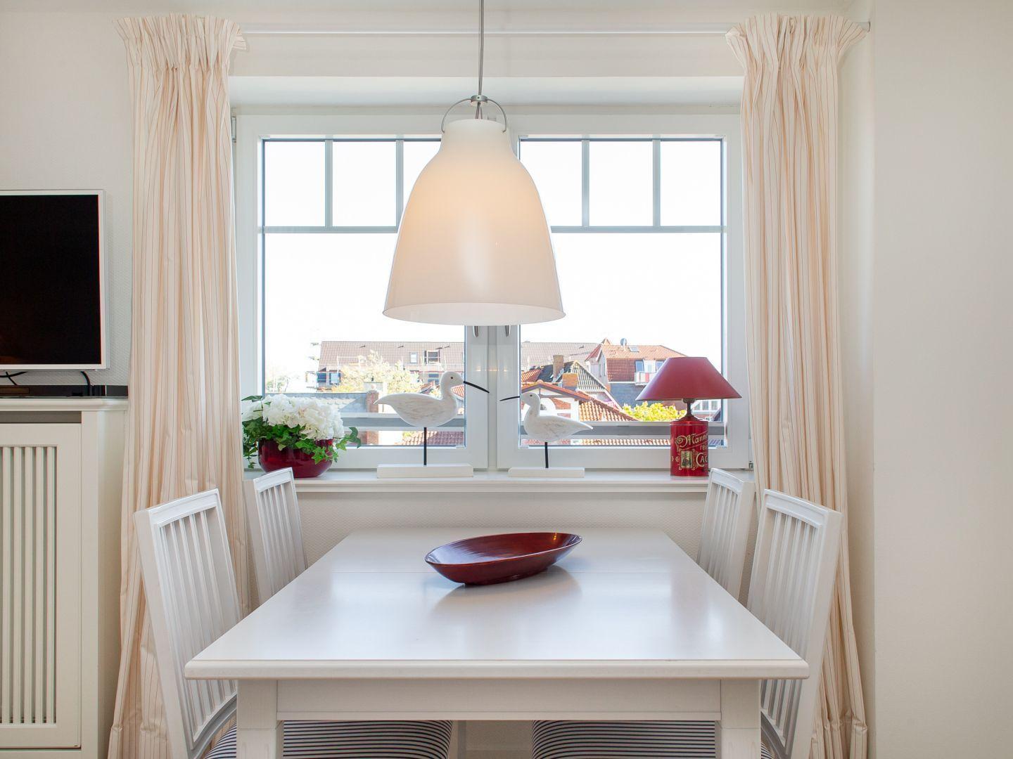 Esszimmer mit weißem Tisch, Stühlen und Fensterblick auf Dächer.