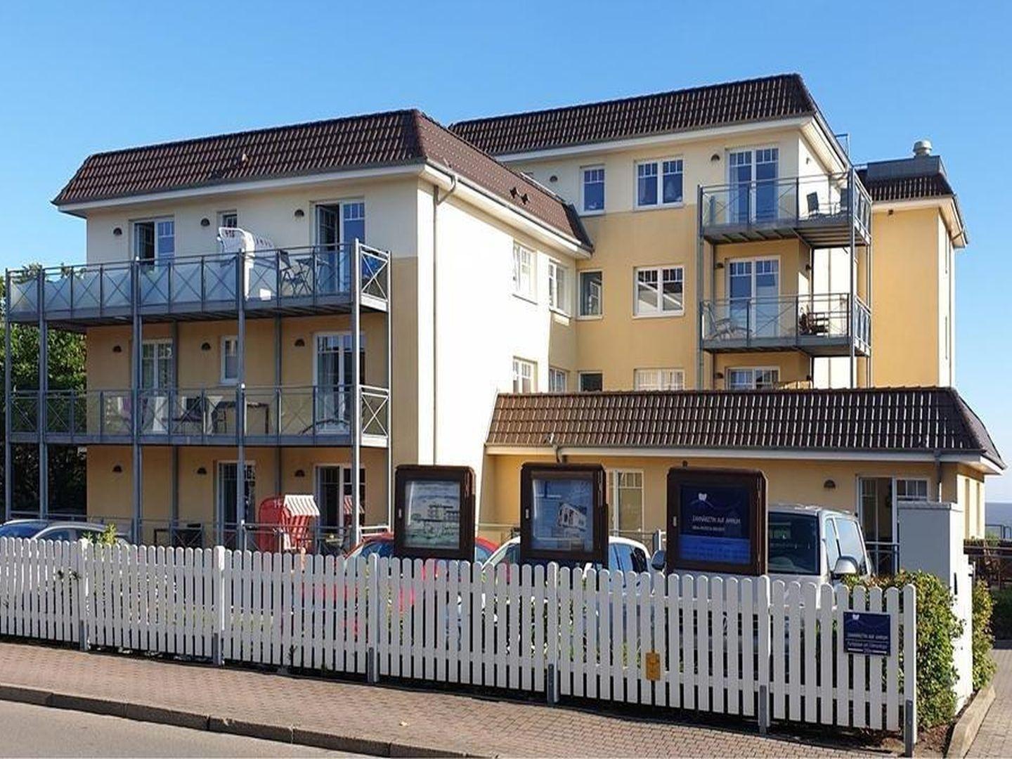 Ferienhaus mit Balkonen und weißen Zaun im Vordergrund.