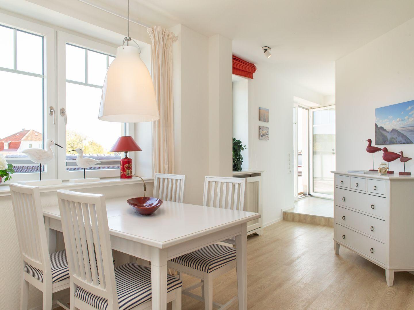 Esszimmer mit weißem Tisch, Stühlen und Fenster. Hintergrund: weiße Wände und Holzboden.