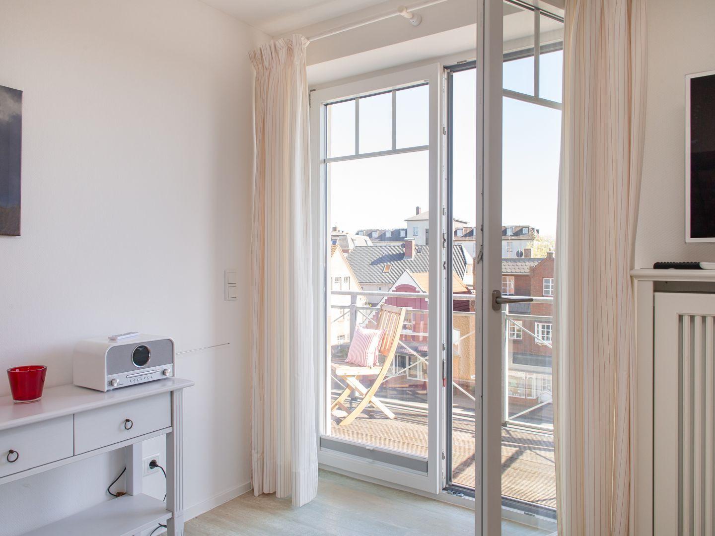 Zimmer mit Balkon, Blick auf Dächer, weiße Wände, Schrank und Radio.