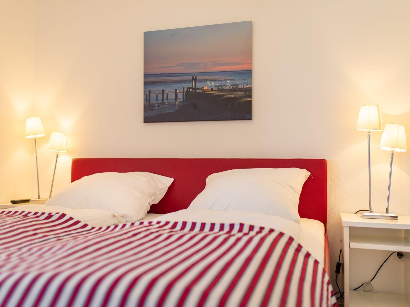 Schlafzimmer mit rotem Kopfteil, gestreifter Bettdecke und Wandbild über dem Bett.